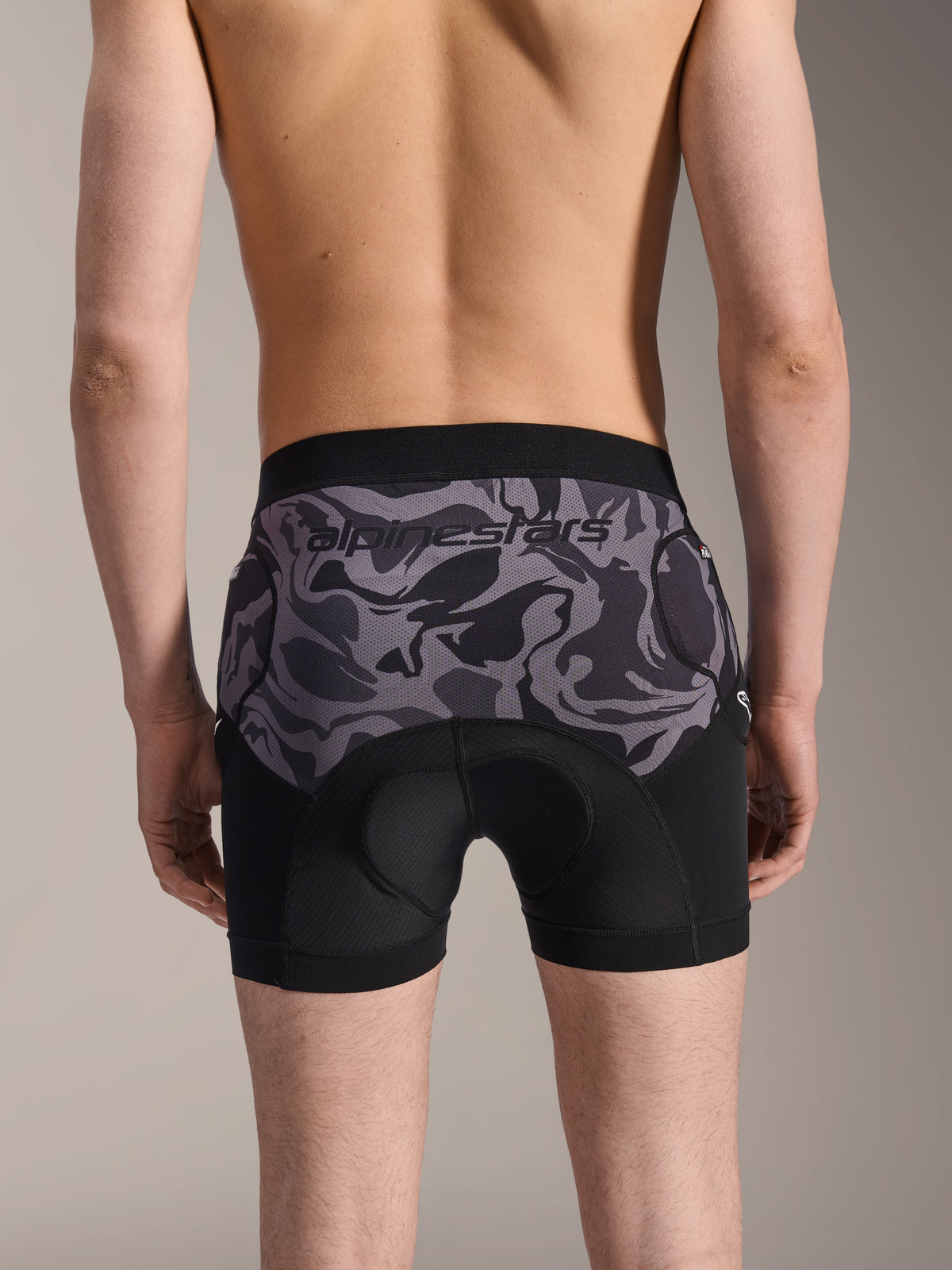 Alpinestars A-Motion Plasma Protection Boxers, ochronne szorty MTB, kolor Black Camo, widok z tyłu na modelu, logo Alpinestars na siatkowym panelu moro, zintegrowana wkładka z irchy i kieszenie na ochraniacze bioder, oddychająca warstwa bazowa do jazdy terenowej