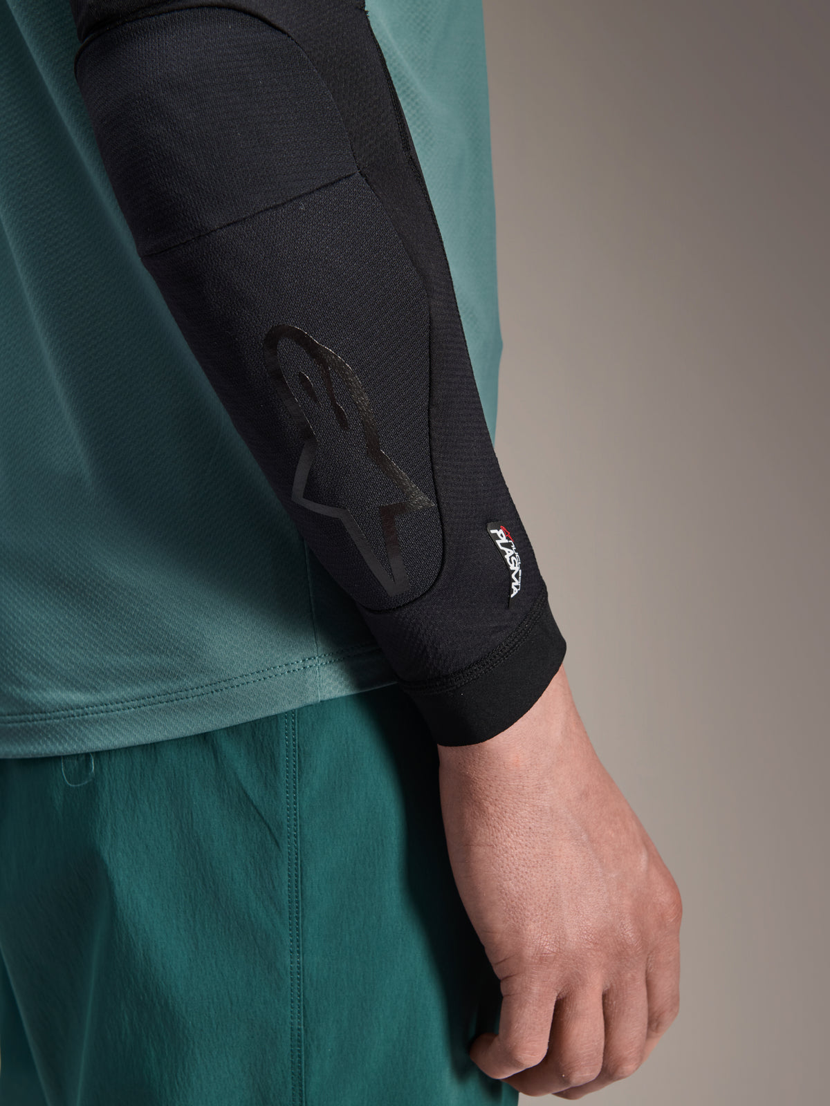 Alpinestars A-Motion Plasma Elbow Sleeve, czarny ochraniacz na łokieć MTB, zbliżenie na ramię w morskiej koszulce, tonalne logo Astars i branding Nucleon Plasma, smukła konstrukcja z siatki do jazdy terenowej