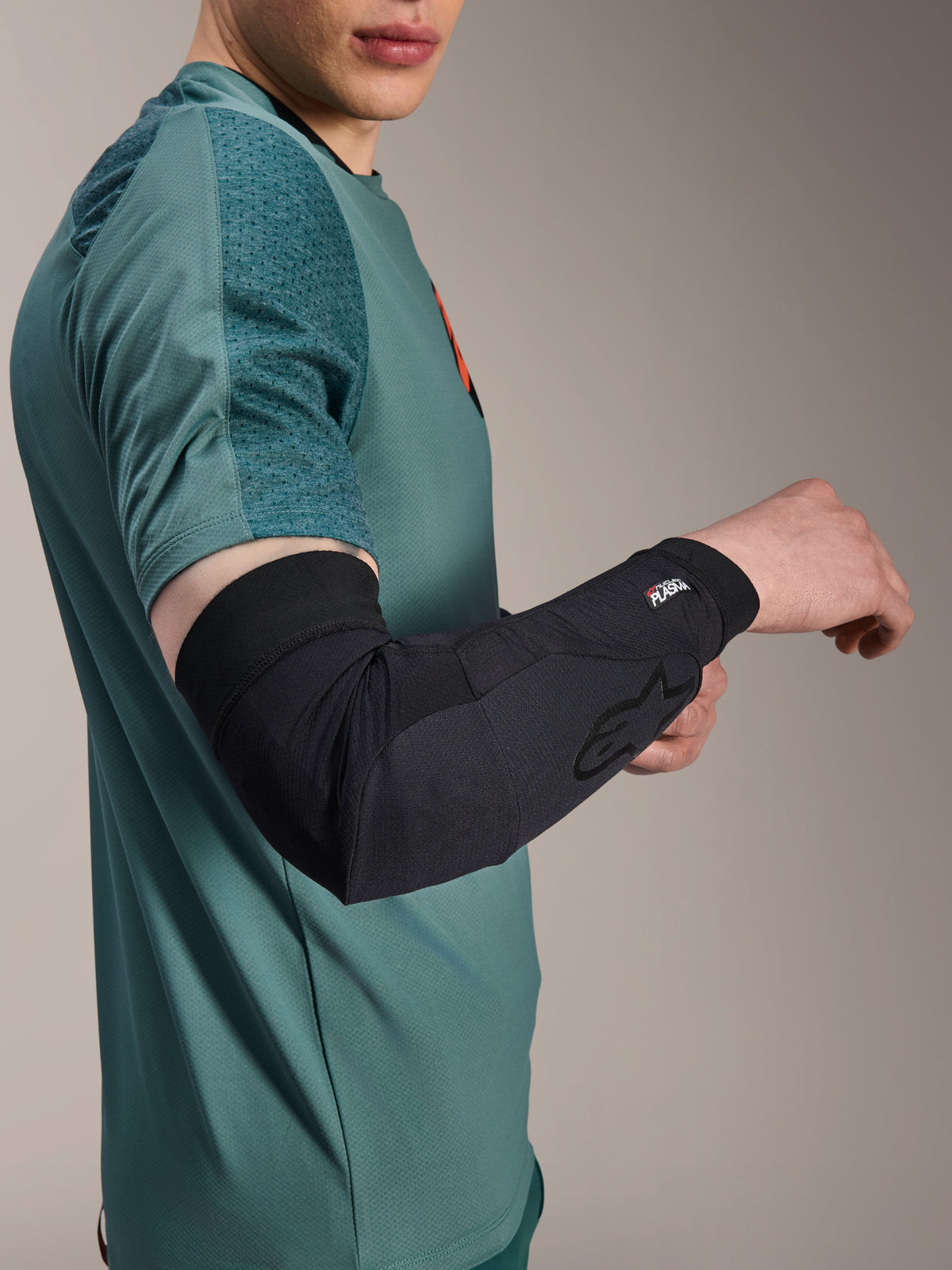 Alpinestars A-Motion Plasma Elbow Sleeve, rowerowy ochraniacz łokcia, czarny, noszony przez rowerzystę w morskiej koszulce, z logo Alpinestars i brandingiem Nucleon Plasma, smukła i oddychająca konstrukcja dla ochrony MTB