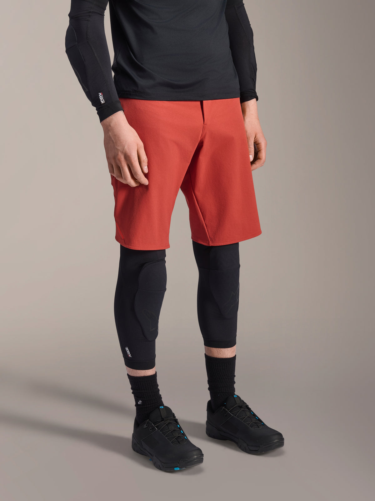 Alpinestars A-Motion Plasma Knee Sleeve, MTB Knee Protector, Black, worn with red shorts and black mountain bike shoes, low-profile slip-on design featuring contoured protective pads and breathable mesh.