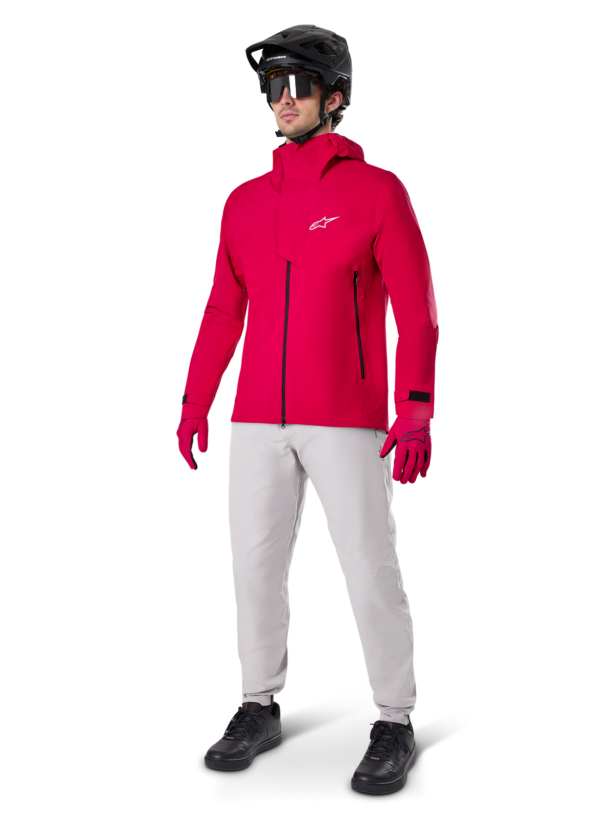 Model wearing Alpinestars A-Dura Waterproof Pants in Titanium gray, paired with a bright red waterproof jacket and matching gloves, black mountain bike helmet with goggles, and black shoes, full mountain biking gear for wet trail conditions