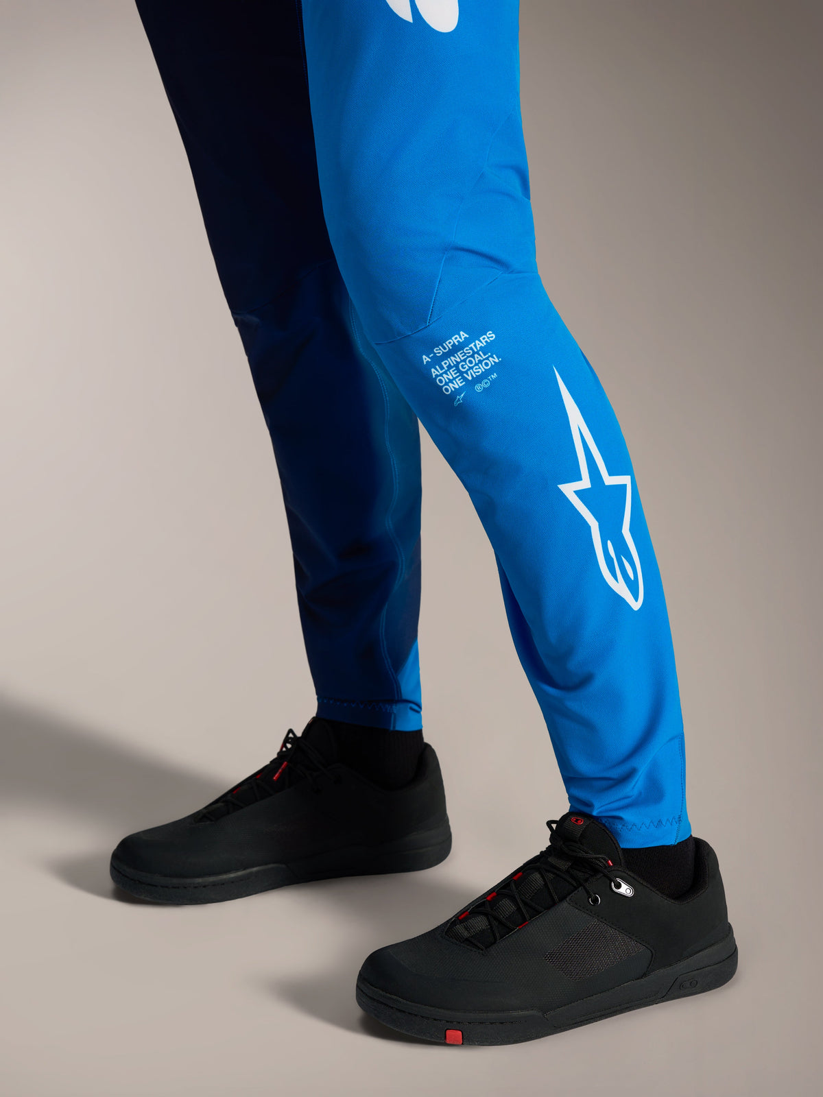 Spodnie Alpinestars A-Supra Elite Faded Bright Blue, białe logo Astars na dolnej części nogawki i czarne buty MTB.