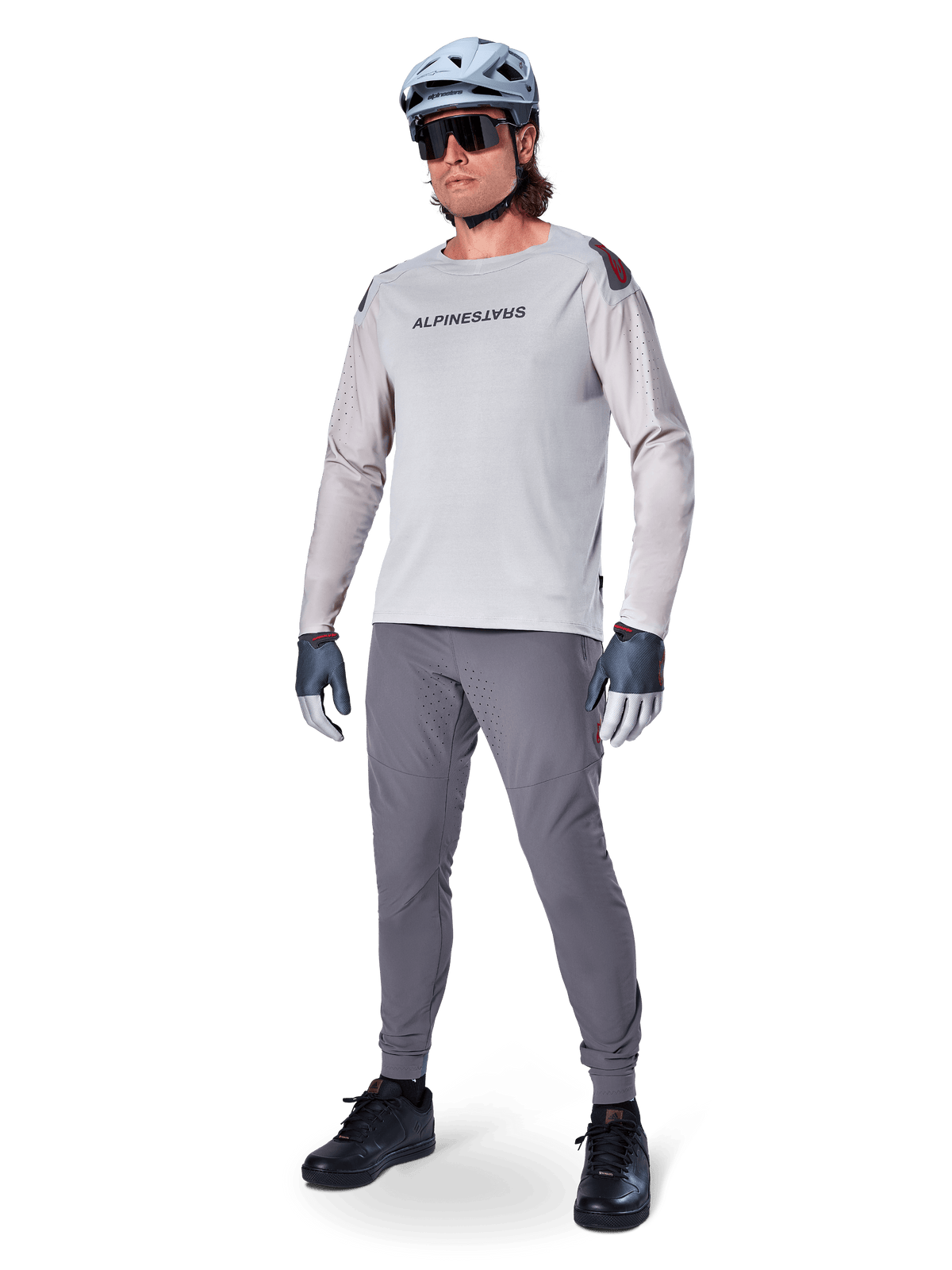 Spodnie Alpinestars A-Aria Elite, ciemnoszare spodnie MTB, noszone przez rowerzystę w jasnoszarej koszulce z długim rękawem i szarym kasku, z laserowo wycinaną wentylacją na udach i dopasowanym sportowym krojem do kolarstwa górskiego.