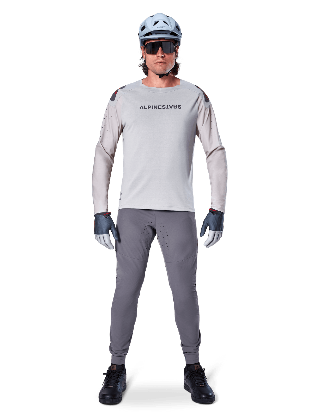 Alpinestars A-Aria Elite Pants, ciemnoszare spodnie rowerowe MTB, noszone przez rowerzystę w jasnoszarej koszulce z długim rękawem, jasnoniebieskim kasku i czarnych butach, z widocznymi laserowymi perforacjami na wewnętrznej stronie nogawek i dopasowanym sportowym krojem.