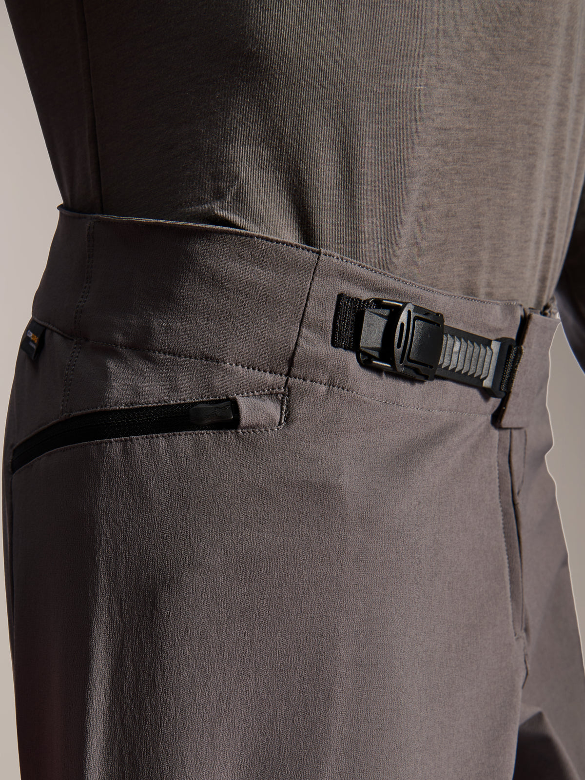 Alpinestars A-Dura Elite Pants, MTB Pants, Dark Gray, close-up view showing the front ratchet closure system and zippered pocket, technical cycling gear for mountain biking