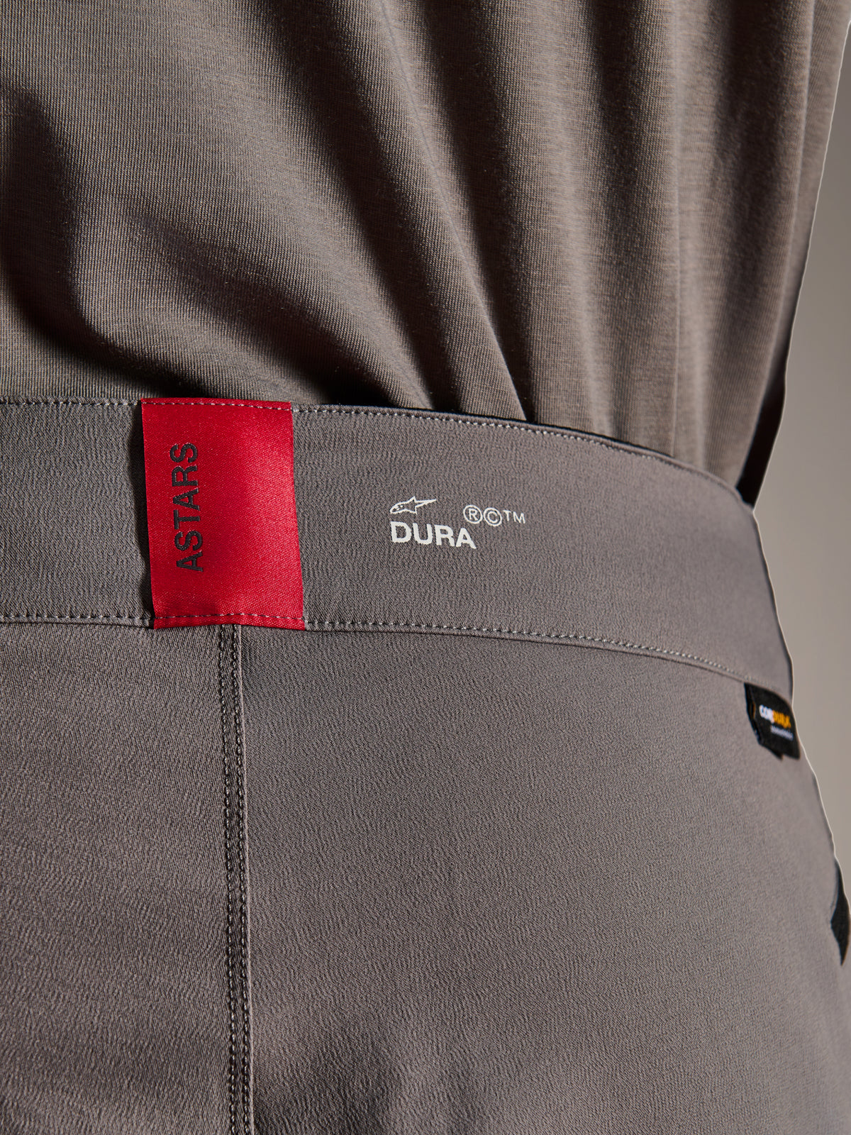 Alpinestars A-Dura Elite Pants, MTB Pants, Dark Gray, close-up of the waistband showing a red ASTARS tag and white DURA logo, featuring textured Cordura fabric and premium branding details.