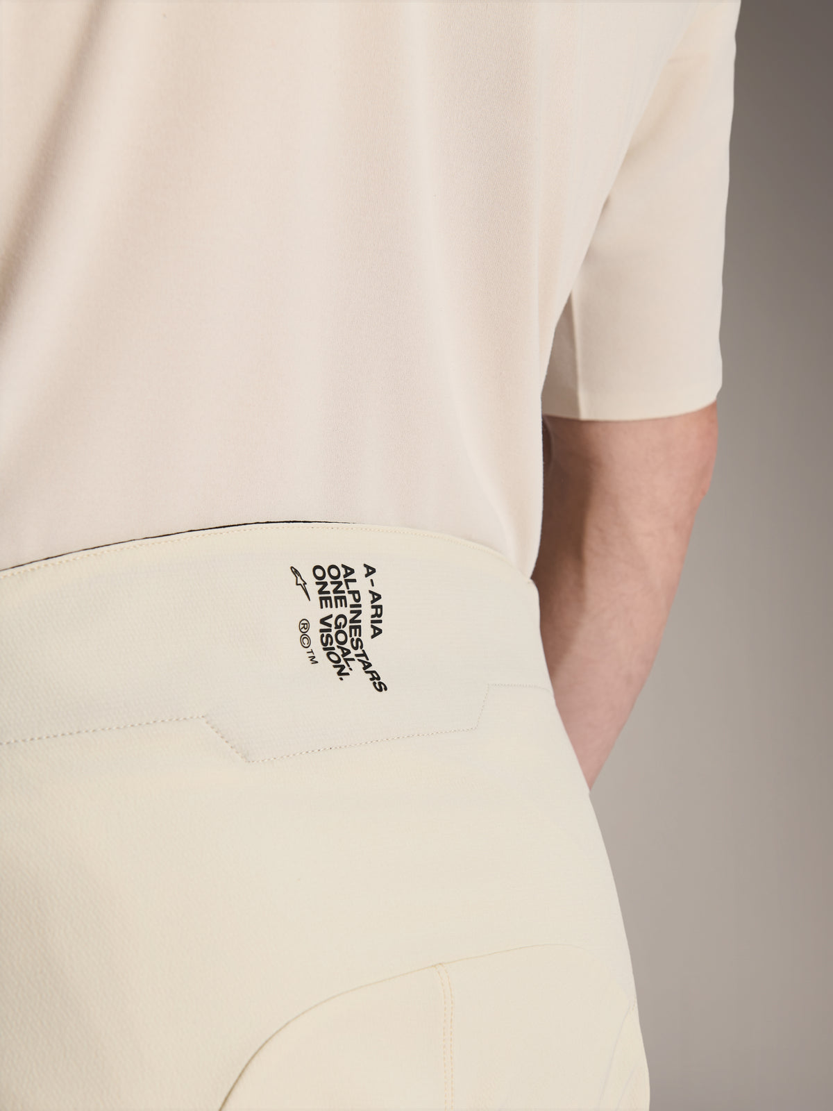 Alpinestars A-Aria Elite Shorts, szorty rowerowe MTB, kolor ecru, zbliżenie na tylną część pasa z czarnym brandingiem „A-ARIA ALPINESTARS ONE GOAL. ONE VISION.”, techniczna odzież rowerowa