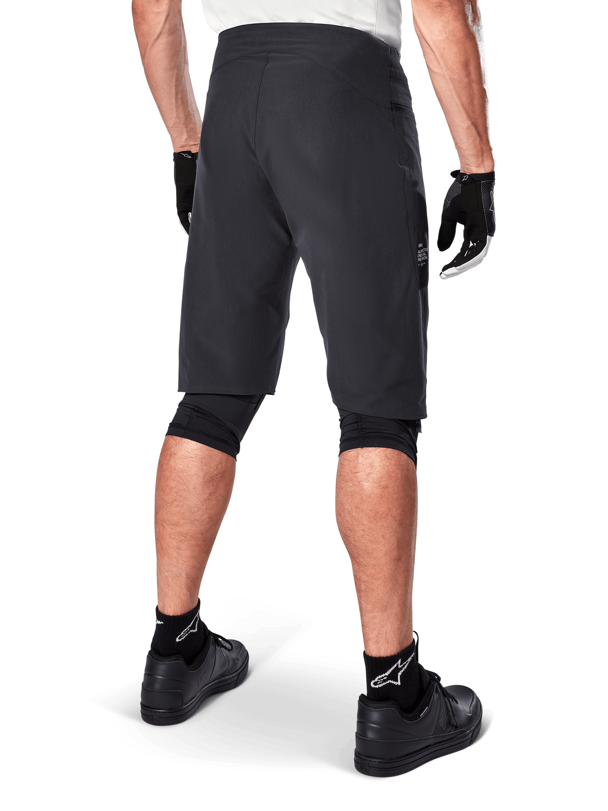 Alpinestars A-Aria Shorts, spodenki rowerowe MTB, czarne, widok z tyłu prezentujący sportowy krój i minimalistyczny design, zestawione z czarnymi rękawiczkami i skarpetami z białym logo Astars, techniczna odzież rowerowa do jazdy w terenie