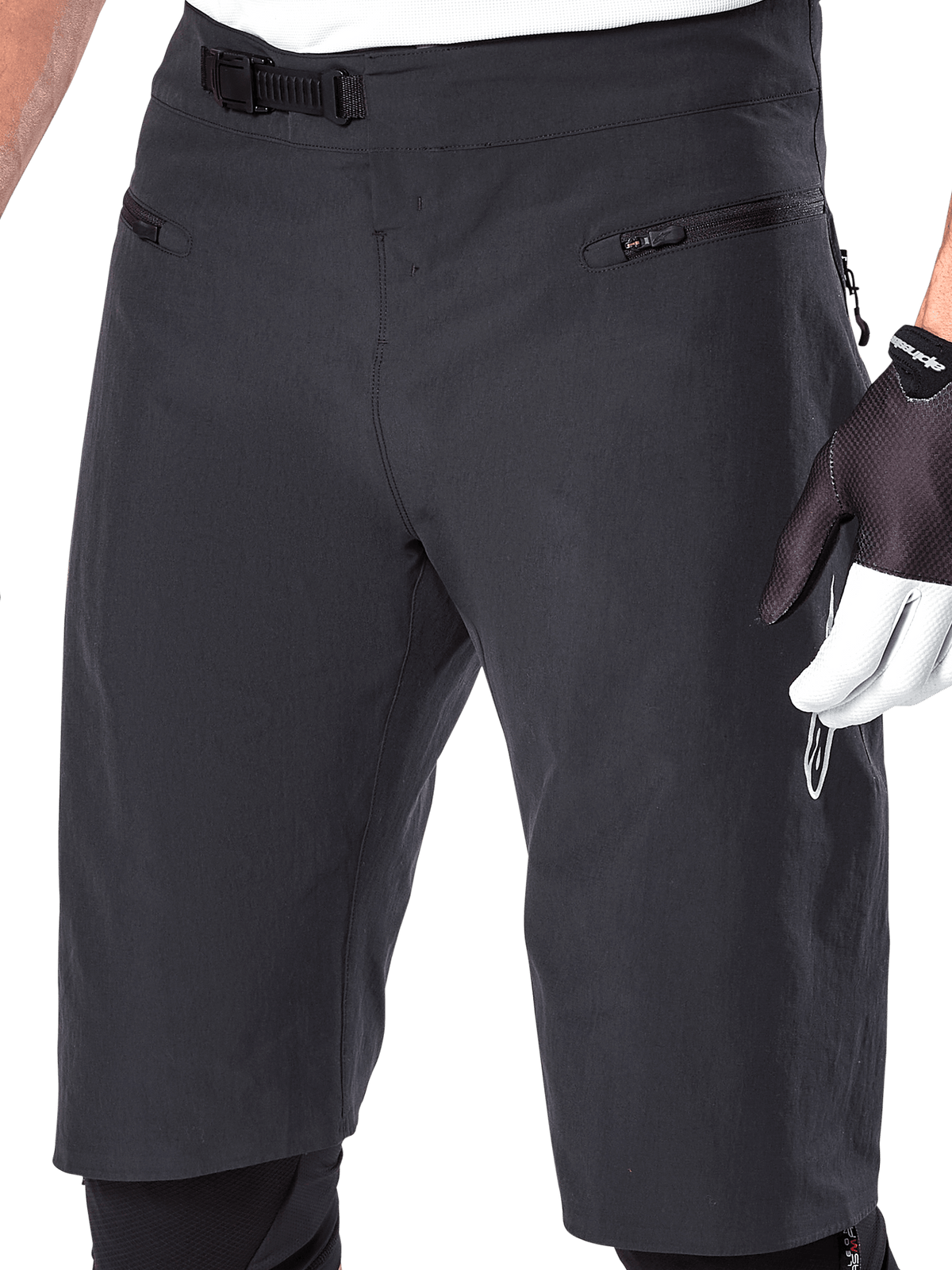 Alpinestars A-Aria Shorts, spodenki rowerowe MTB, czarne, zbliżenie na przód pasa i uda pokazujące system zapięcia zapadkowego oraz kieszenie na zamek, noszone z czarno-białymi rękawiczkami rowerowymi, profesjonalna odzież trailowa
