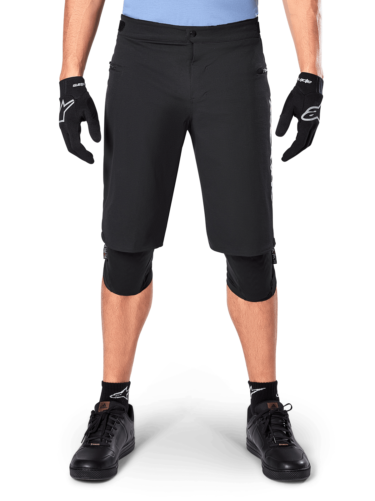 Alpinestars A-Dura Elite Shorts, czarne spodenki rowerowe MTB, noszone przez rowerzystę w czarnych rękawiczkach i ochraniaczach kolan, zapięcie na zatrzask, kieszenie na zamek, wytrzymały materiał Cordura do jazdy w terenie