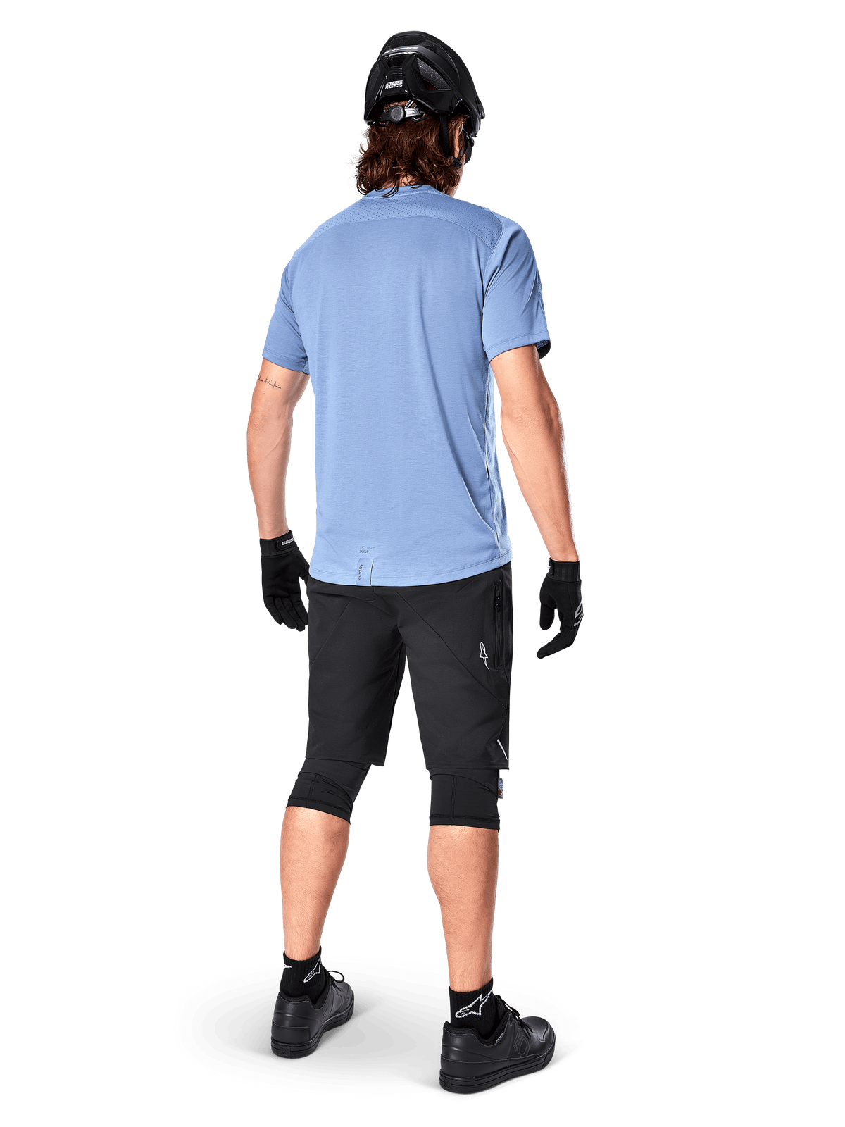 Alpinestars A-Dura Elite Shorts, spodenki rowerowe MTB, czarne, widok z tyłu na modelu, zestaw z jasnoniebieską koszulką z krótkim rękawem i czarnym sprzętem ochronnym, techniczna konstrukcja z kieszeniami na zamek i odblaskowymi detalami do jazdy w terenie