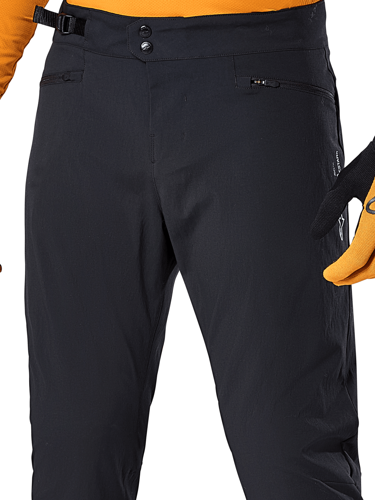 Alpinestars A-Dura Pants, czarne spodnie rowerowe MTB, zbliżenie na podwójne zapięcie na zatrzaski w pasie, boczną regulację dopasowania i kieszenie zapinane na zamek, zestawione z pomarańczową koszulką i rękawicami