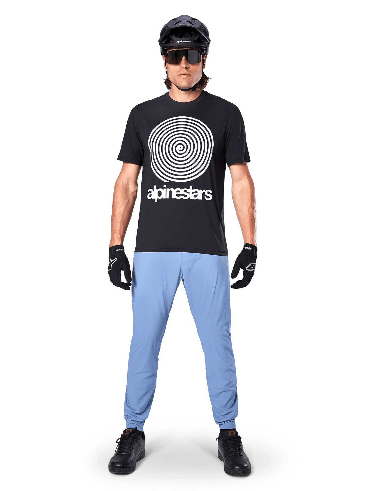 Spodnie Alpinestars A-Dura, Infinity Blue, spodnie MTB noszone z czarną koszulką z grafiką spirali, czarnymi rękawicami i czarnym kaskiem, wykonane z trwałej, elastycznej tkaniny z elastycznymi mankietami, profesjonalna odzież na rower górski
