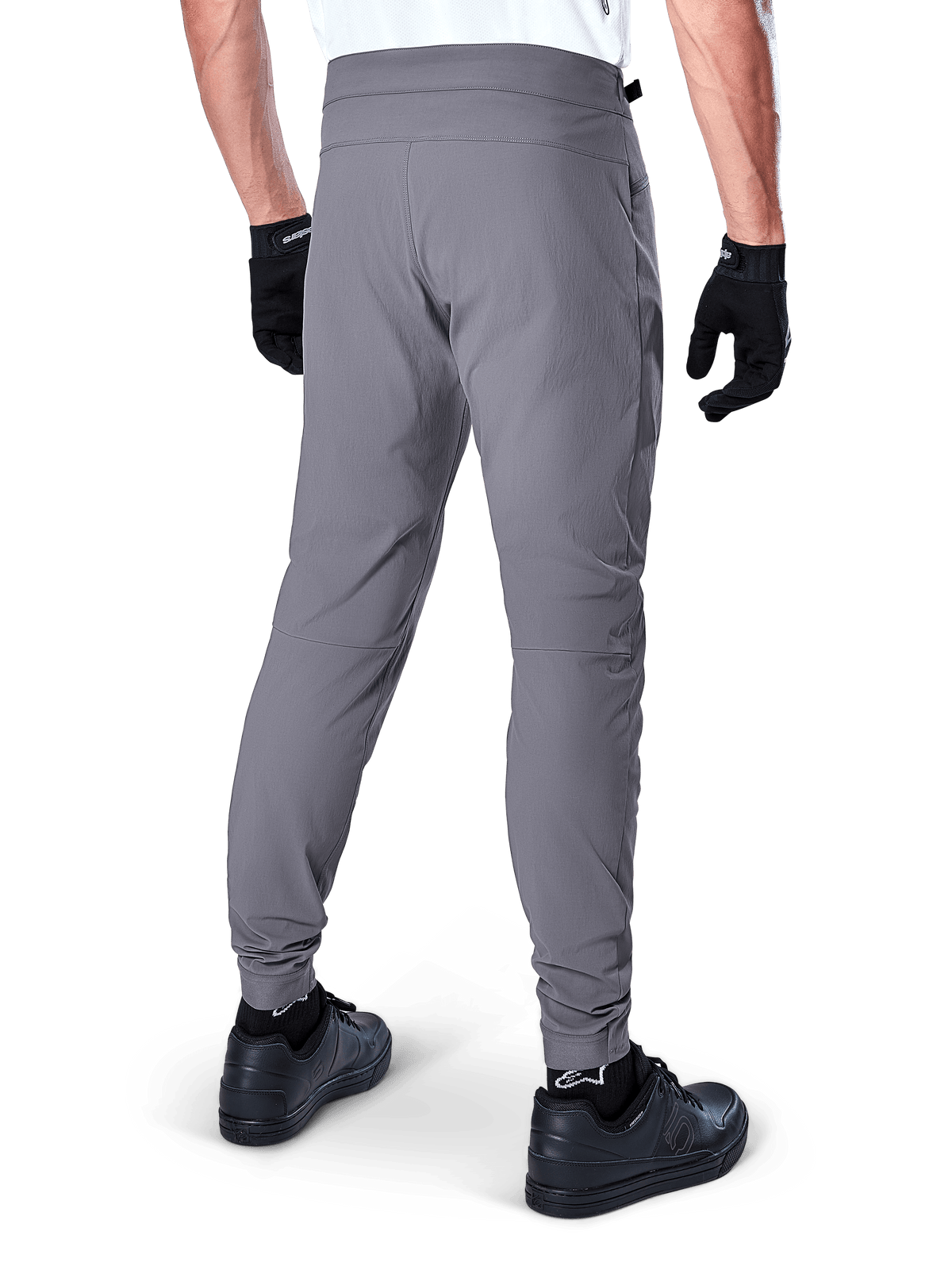 Alpinestars A-Dura Pants, spodnie rowerowe MTB, ciemnoszare, widok z tyłu modelu, wykonane z trwałej dwukierunkowej tkaniny rozciągliwej z elastycznymi mankietami, zestawione z czarnymi rękawiczkami i butami sportowymi dla wyglądu gotowego do jazdy na rowerze
