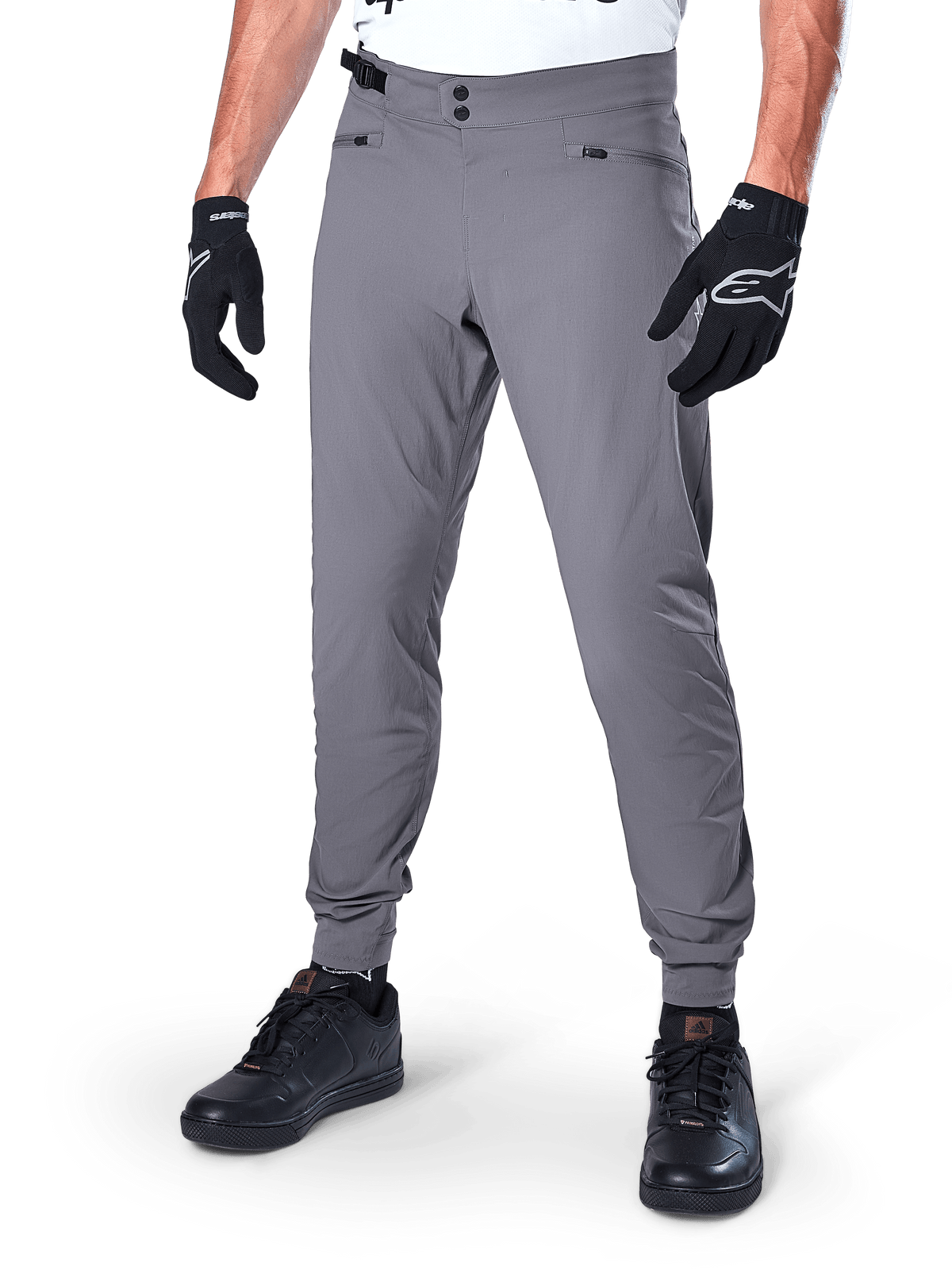 Alpinestars A-Dura Pants, ciemnoszare spodnie MTB, z podwójnym zapięciem na zatrzaski w pasie i kieszeniami na suwak, elastyczne mankiety, noszone z czarnymi rękawicami rowerowymi i czarnymi sneakersami