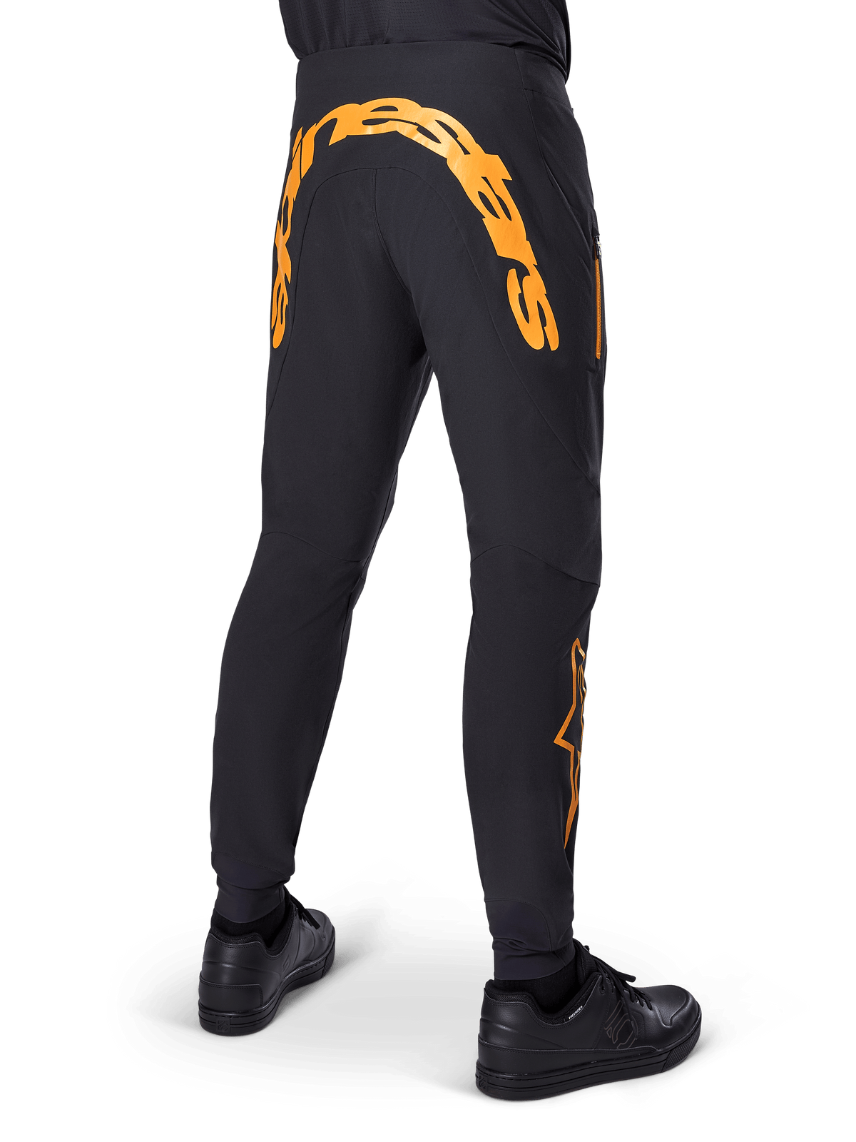 Alpinestars A-Supra Race Pants, czarne spodnie MTB, widok z tyłu z dużym pomarańczowym napisem Alpinestars na karczku, pomarańczowe logo na dolnej części nogawki, sportowy krój z kieszenią na zamek, czarne buty