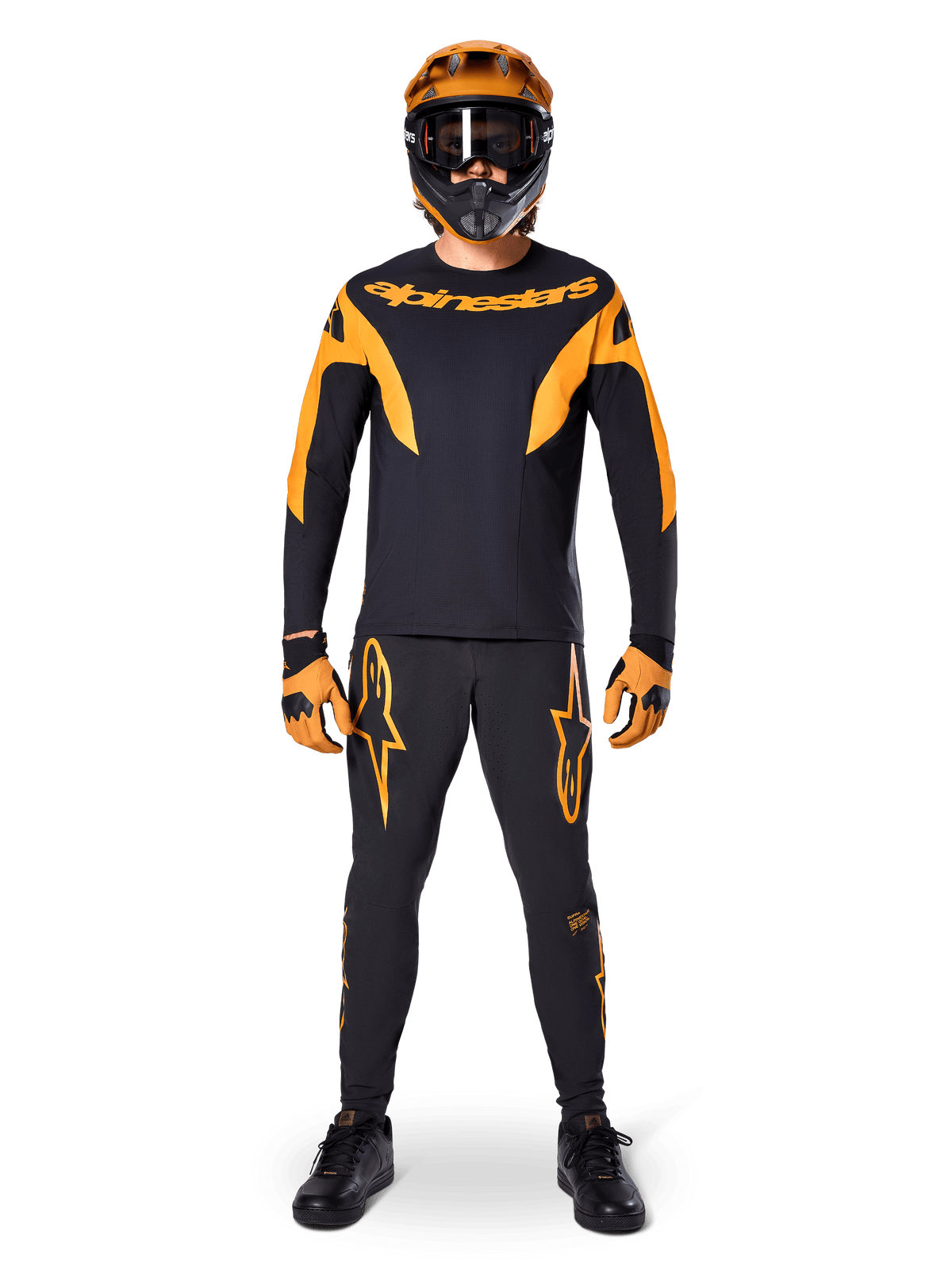 Alpinestars A-Supra Race Pants, spodnie wyścigowe MTB, czarno-pomarańczowe, prezentowane na zawodniku w pełnym stroju wyścigowym z czarno-pomarańczową koszulką, pomarańczowym kaskiem i dopasowanymi rękawicami, z dużymi pomarańczowymi logotypami gwiazdy na nogawkach