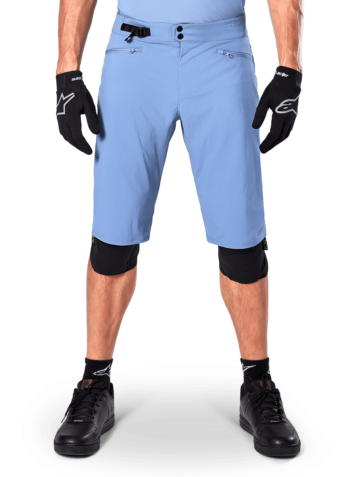 Alpinestars A-Dura Shorts, spodenki do kolarstwa górskiego w kolorze Infinity Blue, noszone z czarnymi rękawiczkami i nakolannikami, wyposażone w podwójne zapięcie na napy i boczną regulację w talii, wyczynowa odzież rowerowa do MTB