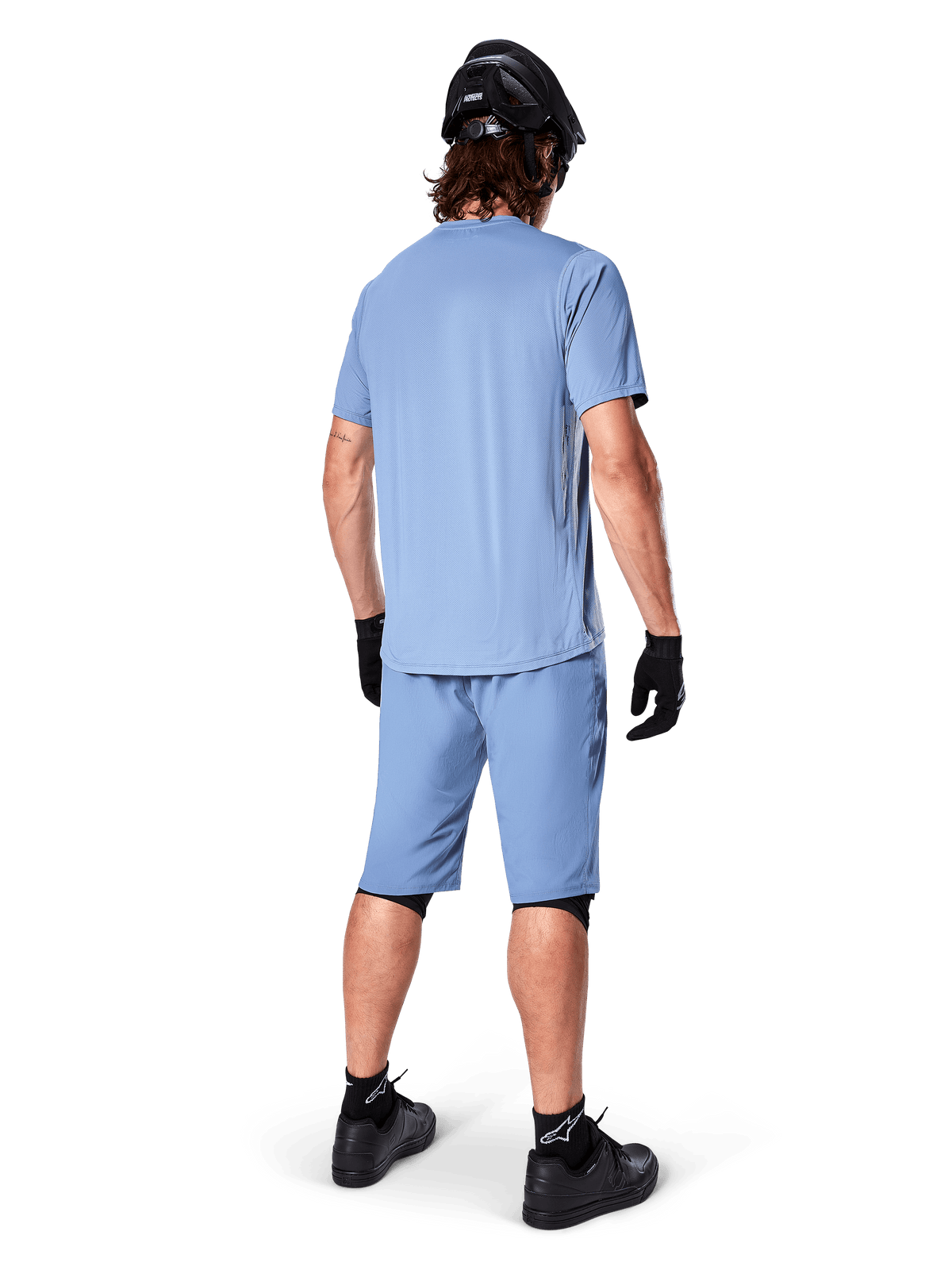 Widok z tyłu rowerzysty górskiego ubranego w spodenki Alpinestars A-Dura w kolorze Infinity Blue, pasującą koszulkę z krótkim rękawem, czarny kask, czarne rękawiczki i czarne buty, skoordynowana odzież wyczynowa do jazdy na szlakach MTB