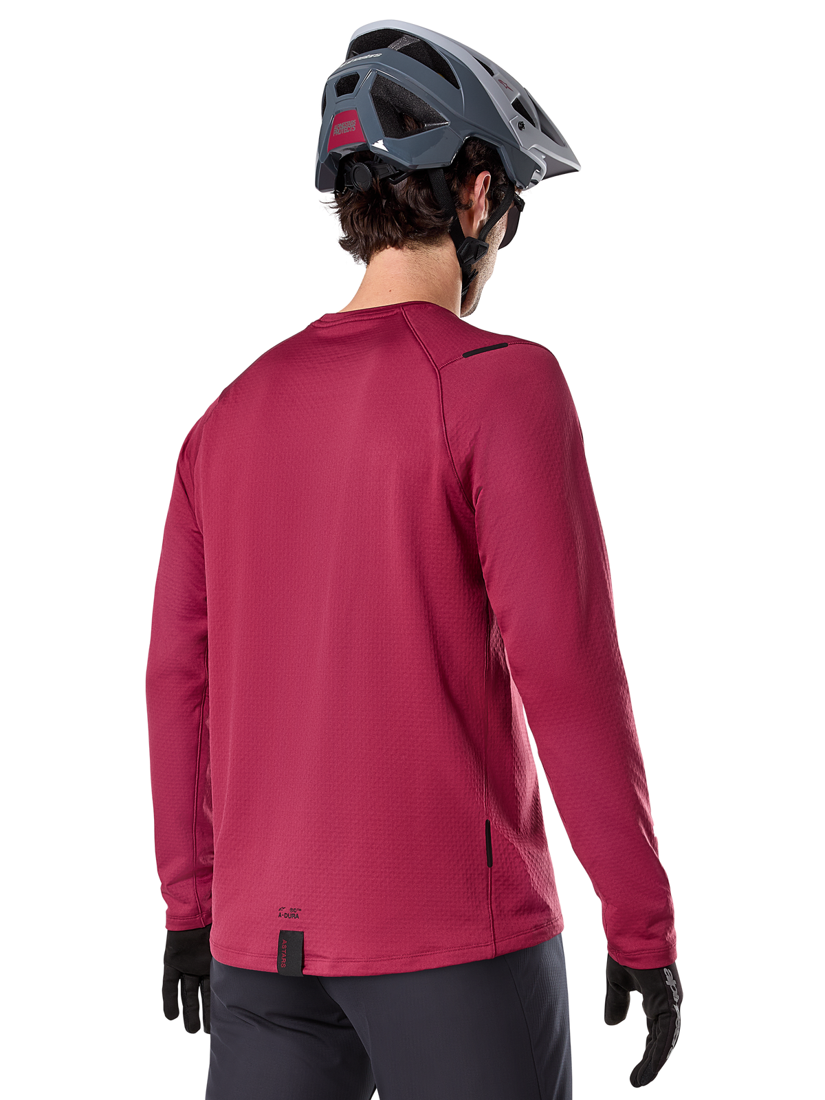 Alpinestars A-Dura Thermal Jersey, koszulka termiczna MTB z długim rękawem, bordowa, widok od tyłu na modelu w szarym kasku MTB i czarnych rękawiczkach, przedłużony tył i małe detale z logo, przeznaczona do jazdy w chłodne dni.