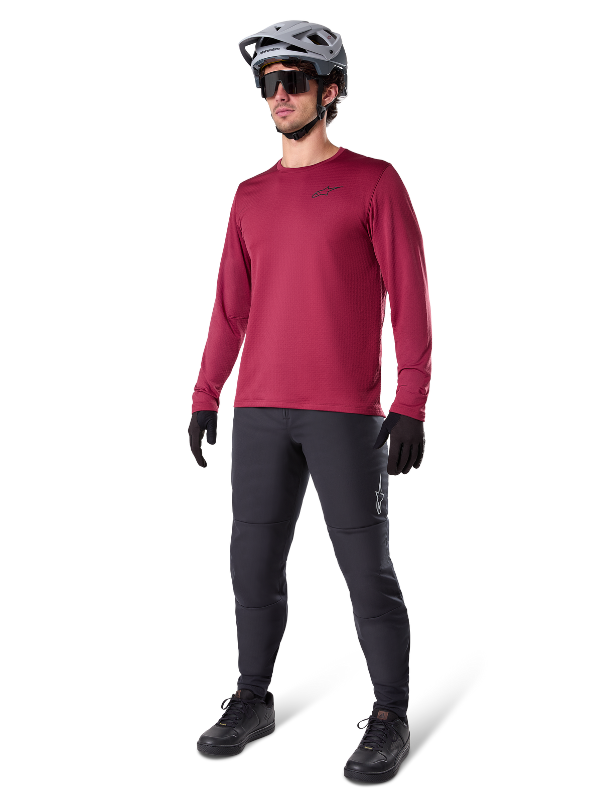Alpinestars A-Dura Thermal Jersey w kolorze bordowym, ocieplana koszulka rowerowa z długim rękawem noszona z ciemnoszarymi spodniami MTB, czarnymi rękawiczkami i szarym kaskiem, ujęcie studyjne całej sylwetki odzieży rowerowej na zimne dni