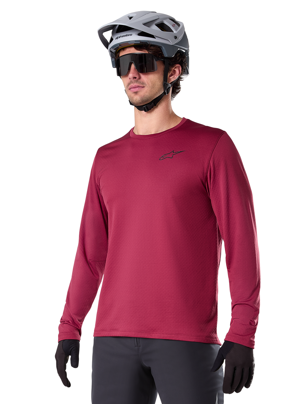 Alpinestars A-Dura Thermal Jersey, koszulka rowerowa MTB z długim rękawem, bordowa, z izolującą podszewką z polaru i małym czarnym logo na klatce piersiowej, noszona z szarym kaskiem, czarnymi okularami przeciwsłonecznymi i czarnymi rękawiczkami, zaprojektowana do jazdy w chłodne dni