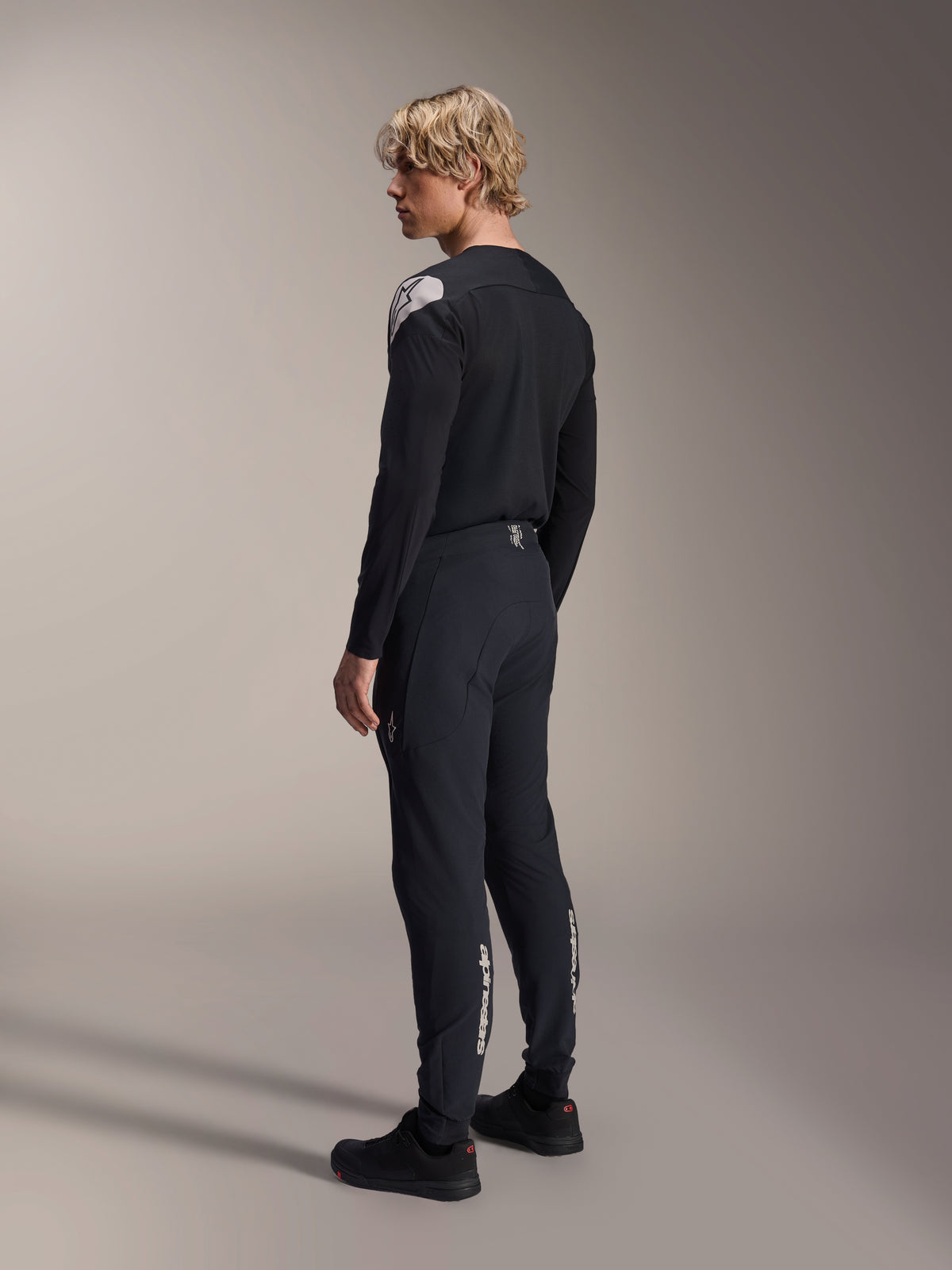 Alpinestars A-Aria Elite Pants, Mountain Bike Pants, Black Titanium, rear three-quarter view on model, featuring white Alpinestars branding on the lower legs, performance fit with elastic cuffs, paired with a matching black long-sleeve jersey.
