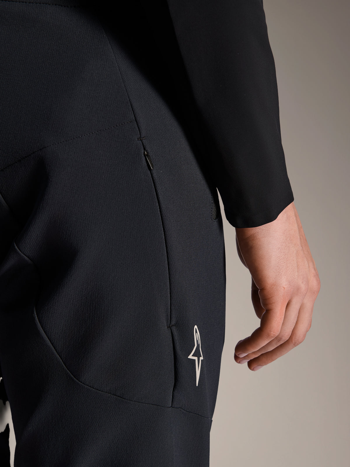 Close-up of Alpinestars A-Aria Elite Pants in Black Titanium, featuring a zippered side pocket and small white star logo, technical mountain bike pants designed for performance cycling