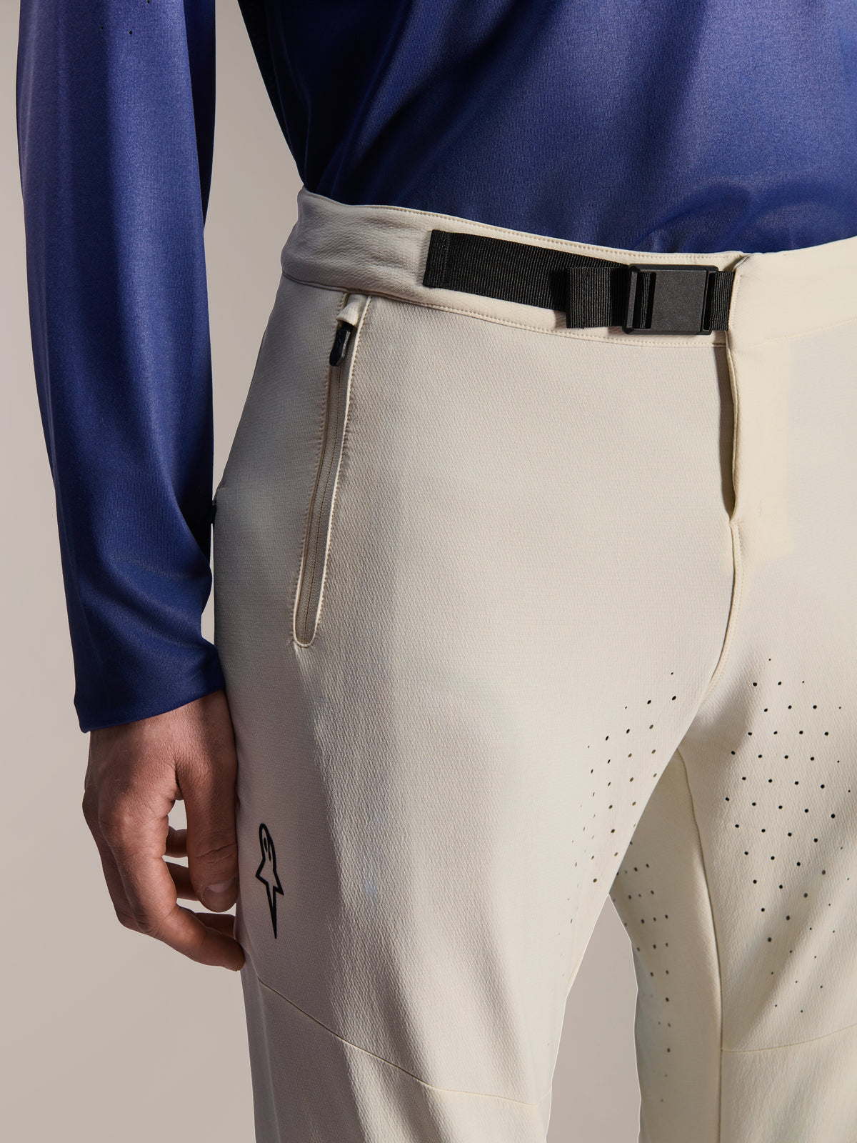 Alpinestars A-Aria Elite Pants, spodnie rowerowe MTB, ecru, zbliżenie na czarną klamrę magnetyczną w pasie, kieszeń zapinaną na zamek i laserowo wycinane otwory wentylacyjne, wyczynowa odzież rowerowa.