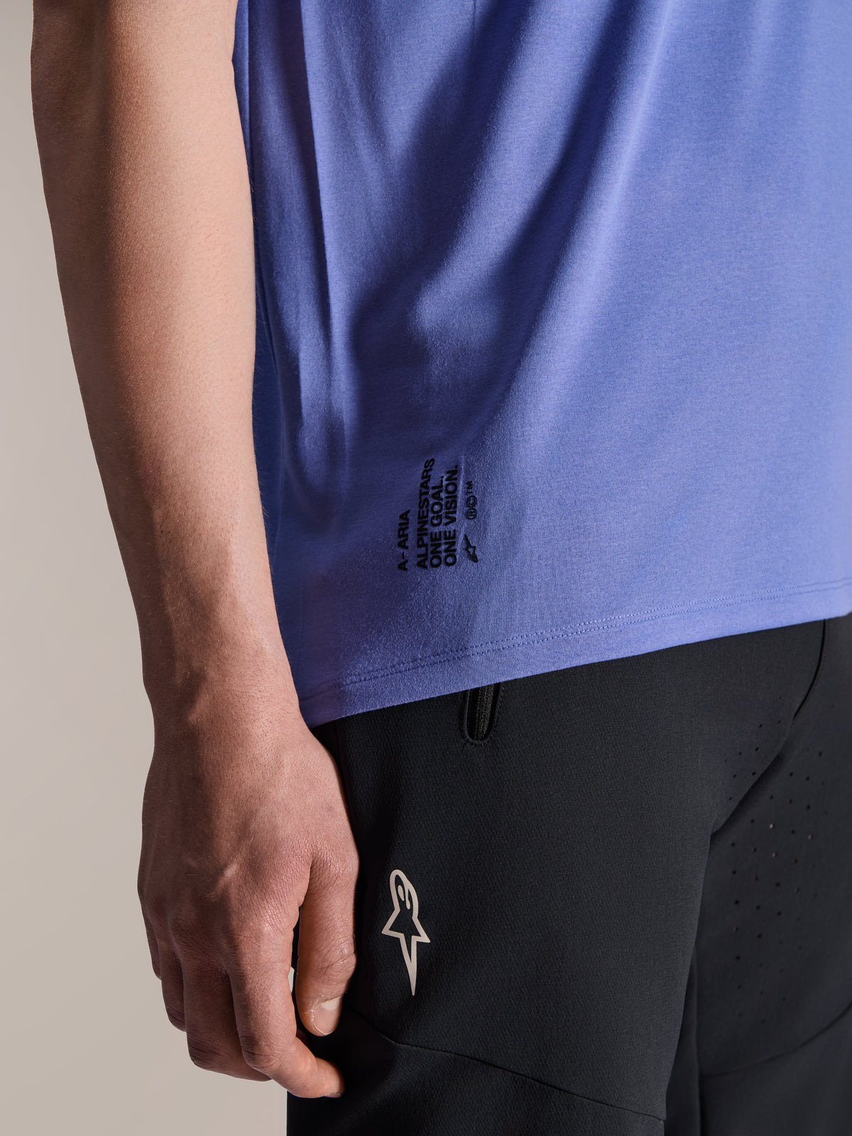 Alpinestars A-Aria Polartec Elite Short Sleeve Jersey w kolorze Baja Blue, detal dolnej bocznej krawędzi z czarnym napisem „One Goal. One Vision.” i logo ASTARS, w zestawieniu z czarnymi spodenkami na rower górski.