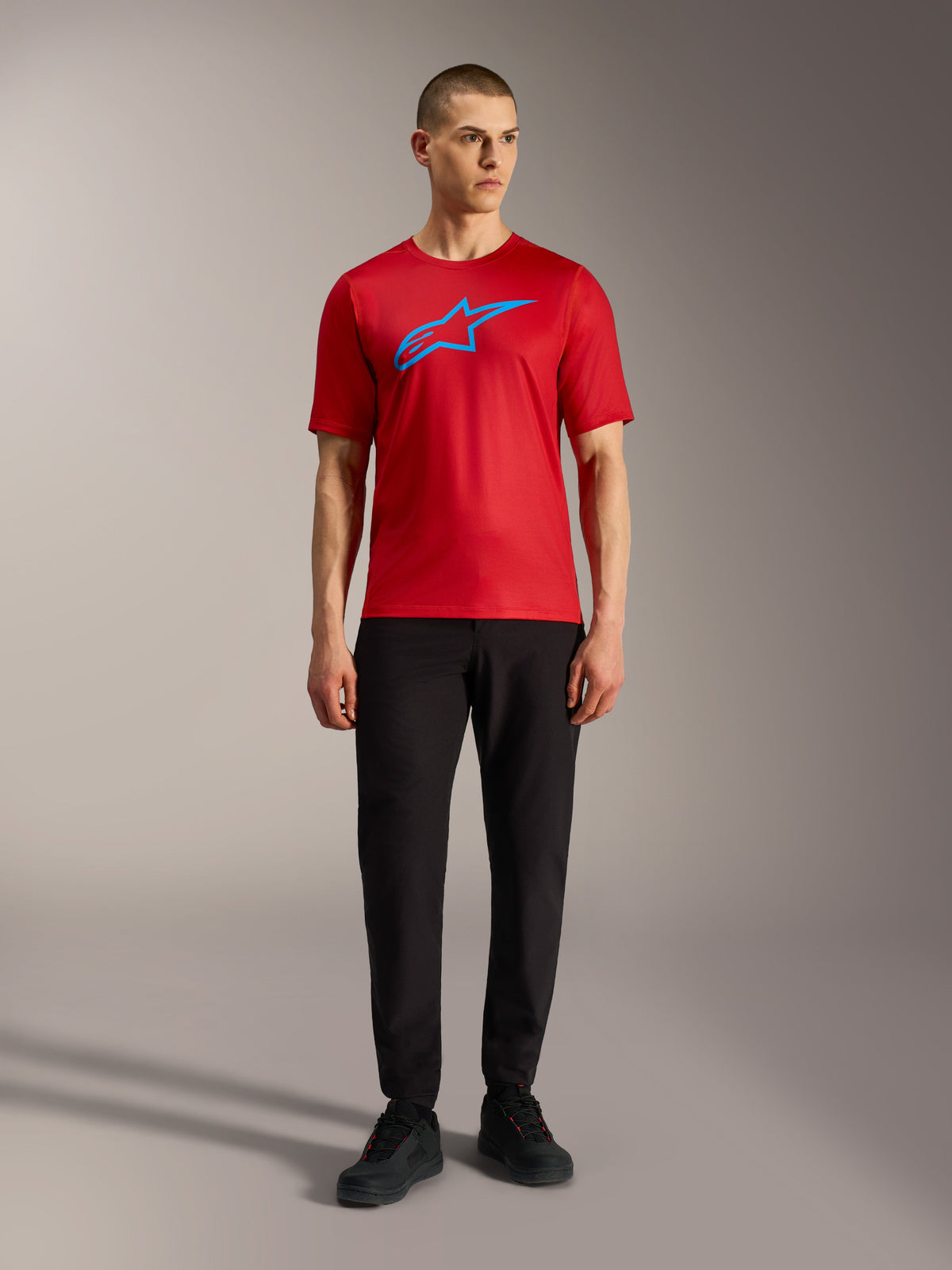 Czerwona koszulka Alpinestars A-Dura Ride z krótkim rękawem i niebieskim logo, czarne spodnie, styl casual MTB.