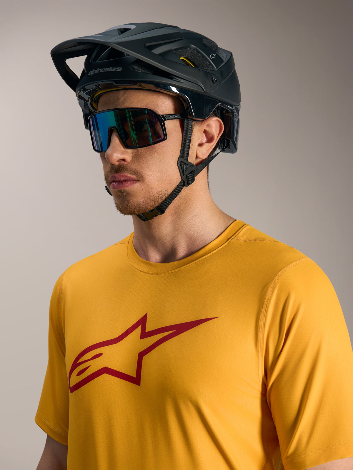 Pomarańczowa koszulka A-Dura Ride z krótkim rękawem, czerwone logo Astars, czarny kask MTB i okulary sportowe.