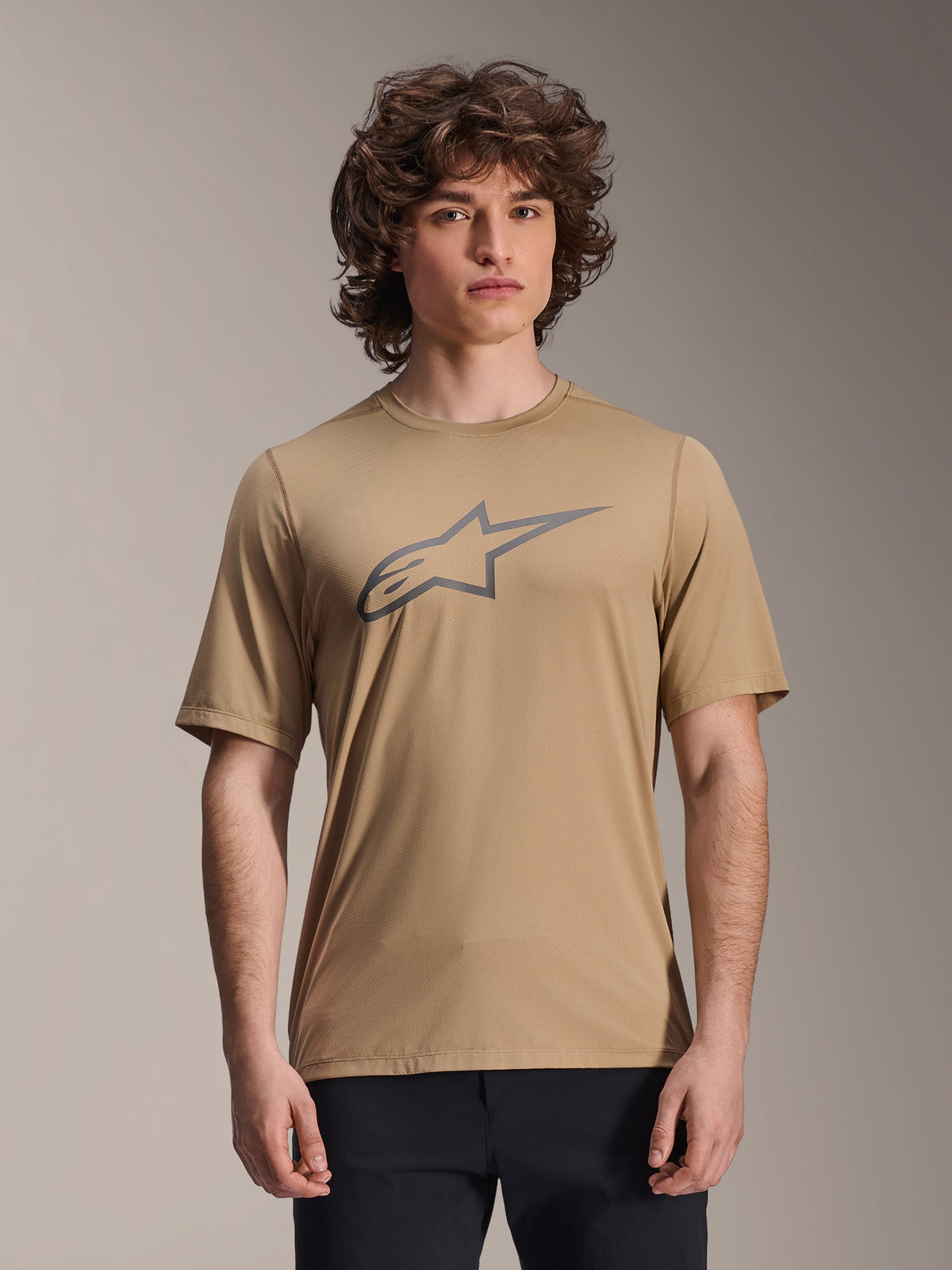 Alpinestars A-Dura Astar Short Sleeve Jersey, jasnobrązowa, noszona przez modela w czarnych spodniach, szare logo Alpinestars w kształcie gwiazdy na piersi, casualowa koszulka MTB do jazdy trailowej