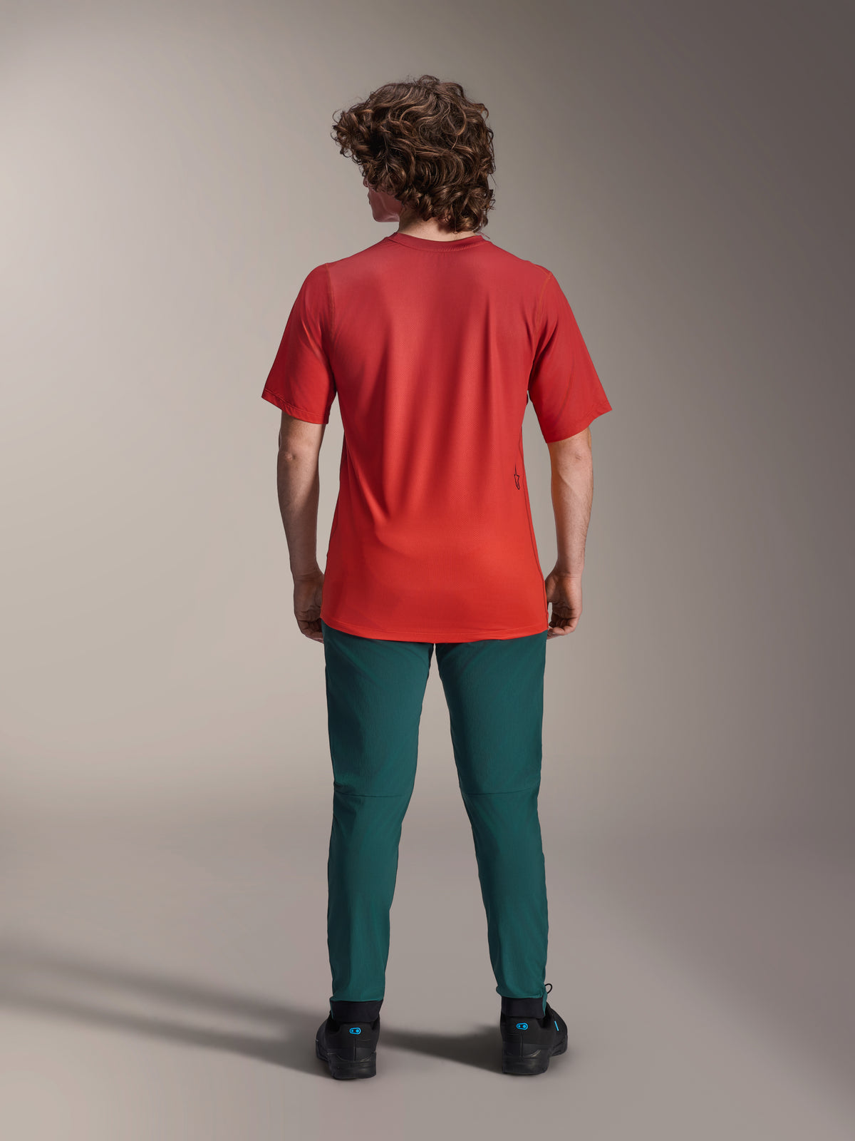 Alpinestars A-Dura Pants w kolorze Dark Pine green, spodnie do kolarstwa górskiego noszone z czerwoną koszulką z krótkim rękawem, widok z tyłu, sportowy krój do kolarstwa terenowego.