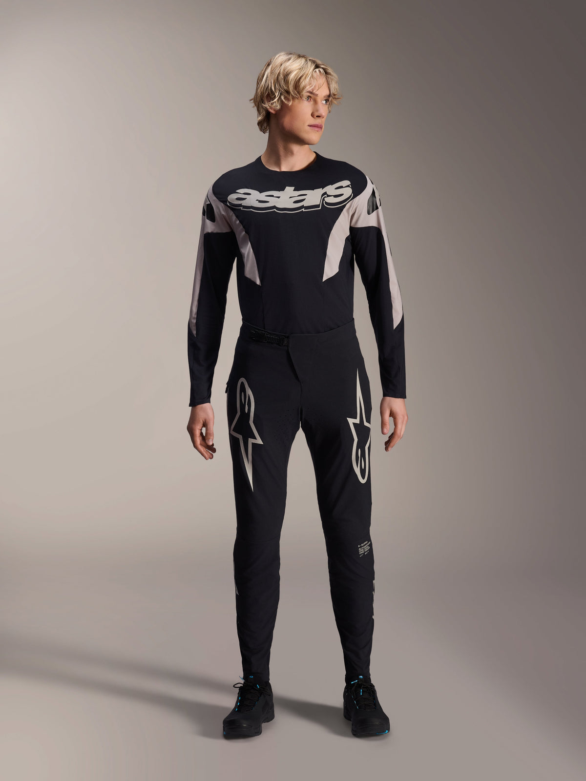 Spodnie Alpinestars A-Supra Melt i pasująca koszulka z długim rękawem, model w czarnym stroju MTB, duże białe grafiki gwiazd na udach, branding „astars” na klatce piersiowej, profesjonalna odzież do wyścigów rowerów górskich