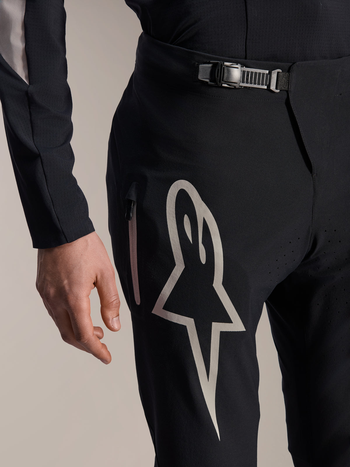 Alpinestars A-Supra Melt Pants, spodnie rowerowe MTB, czarne, z dużym białym logo Astar na udzie, regulowanym zapięciem na zapadkę w pasie i boczną kieszenią na zamek, szczegółowy widok technicznej odzieży MTB