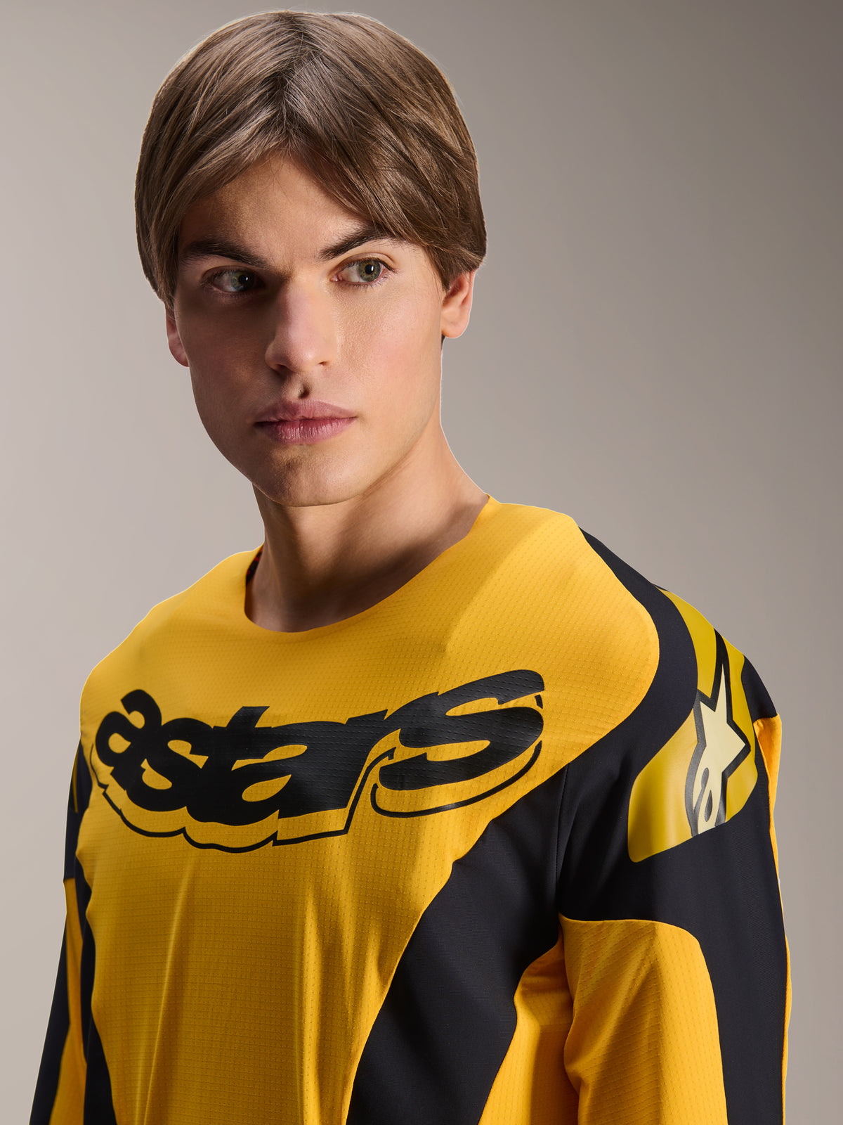 Alpinestars Limited Edition A-Supra Melt Gold Jersey, koszulka MTB z długim rękawem, ciemnożółta z czarnymi grafikami inspirowanymi wyścigami, czarny napis „astars” na klatce piersiowej i logo z gwiazdą na ramieniu, prezentowana na męskim modelu