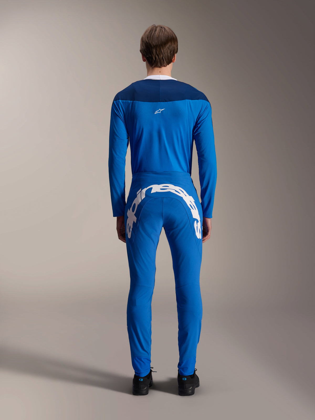 Alpinestars A-Supra Melt Pants, Blue, back view featuring a large white Alpinestars wordmark on the back yoke, worn with a matching blue long-sleeve jersey and black shoes, performance MTB racing gear