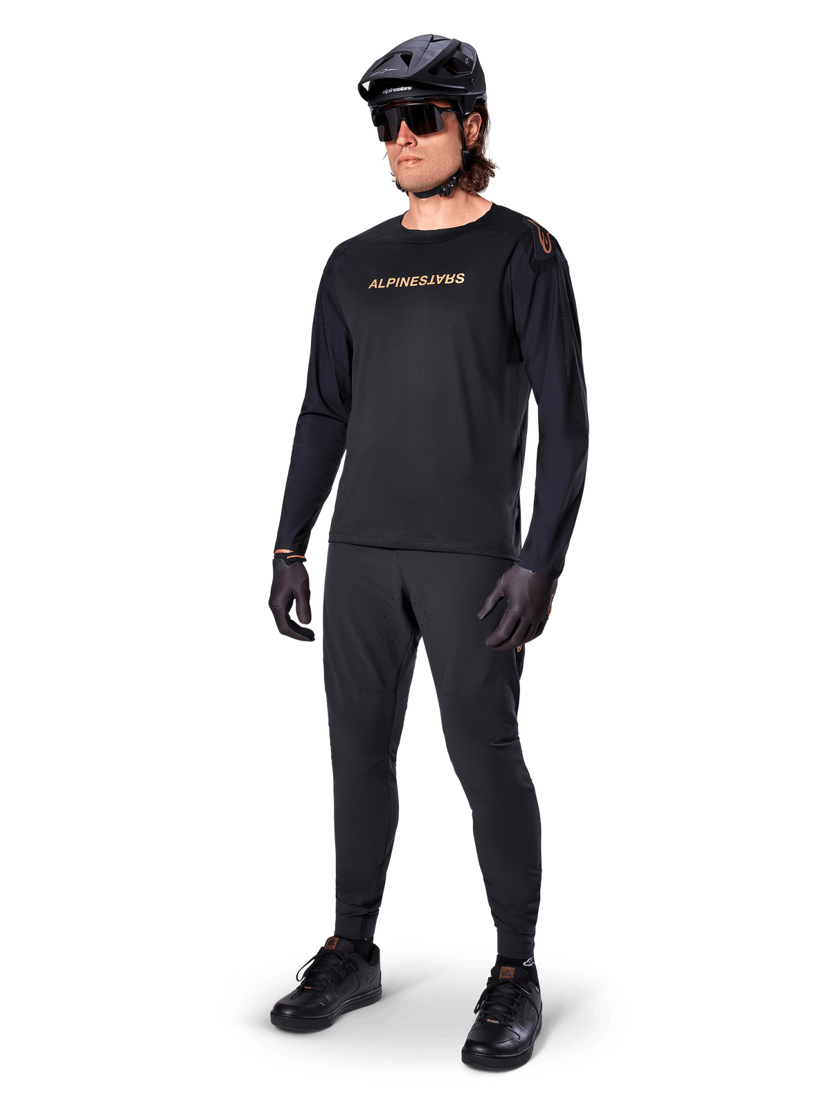 Koszulka z długim rękawem Alpinestars A-Aria Polartec Switch, czarna, brązowe logo na piersi, noszona przez kolarza górskiego w czarnym kasku i okularach przeciwsłonecznych, wydajna odzież rowerowa do jazdy po szlakach