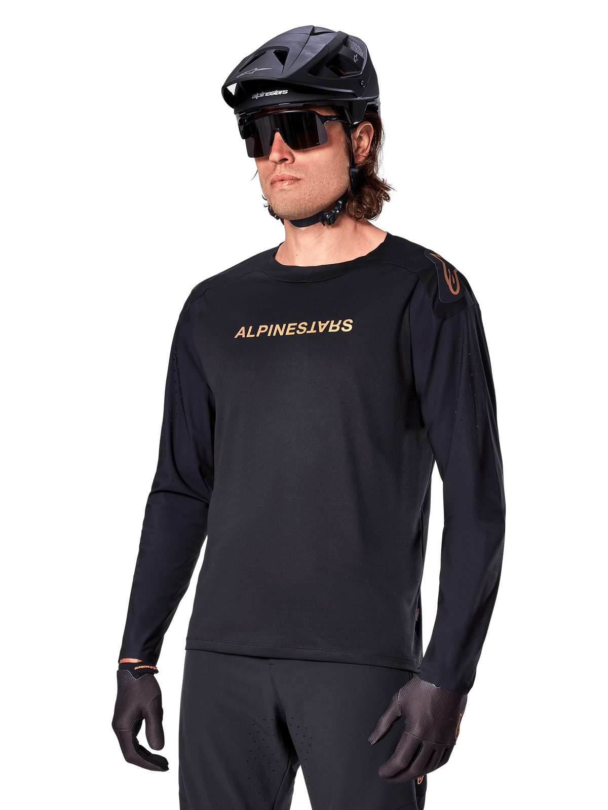 Alpinestars A-Aria Polartec Switch Long Sleeve Jersey, czarna ze złotym logo, odzież do jazdy na rowerze górskim MTB, noszona z czarnym kaskiem i okularami przeciwsłonecznymi, laserowo wycinana wentylacja na rękawach oraz odprowadzający wilgoć materiał Polartec zapewniający wydajność w terenie