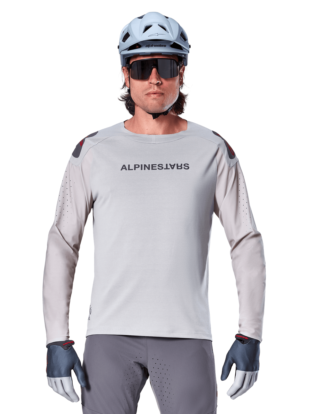 Alpinestars A-Aria Polartec Switch Long Sleeve Jersey, jasnoszara koszulka rowerowa MTB z laserowymi perforacjami na rękawach i logo na klatce piersiowej, noszona z jasnoniebieskim kaskiem, okularami przeciwsłonecznymi i szarymi rękawiczkami