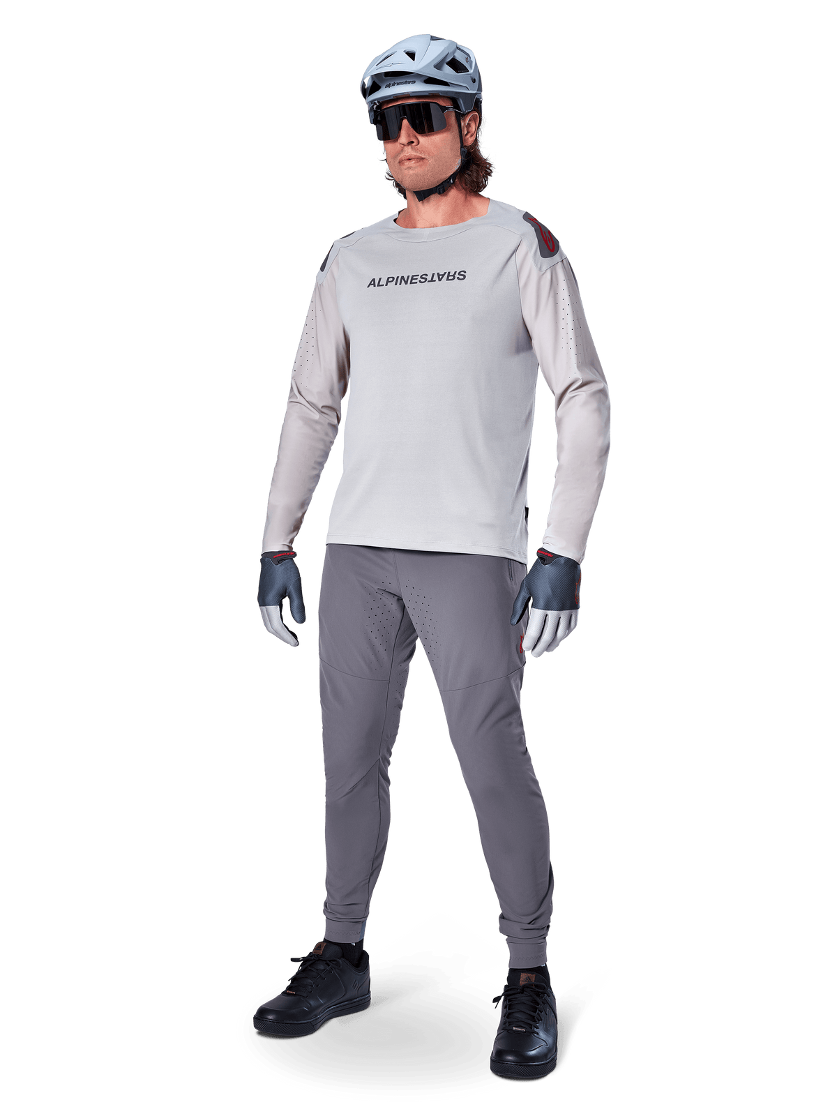 Alpinestars A-Aria Polartec Switch Jersey, koszulka MTB z długim rękawem, jasnoszara, zestawiona z ciemnoszarymi spodniami rowerowymi, kaskiem i rękawicami, laserowo perforowane rękawy i logo Alpinestars na klatce piersiowej.