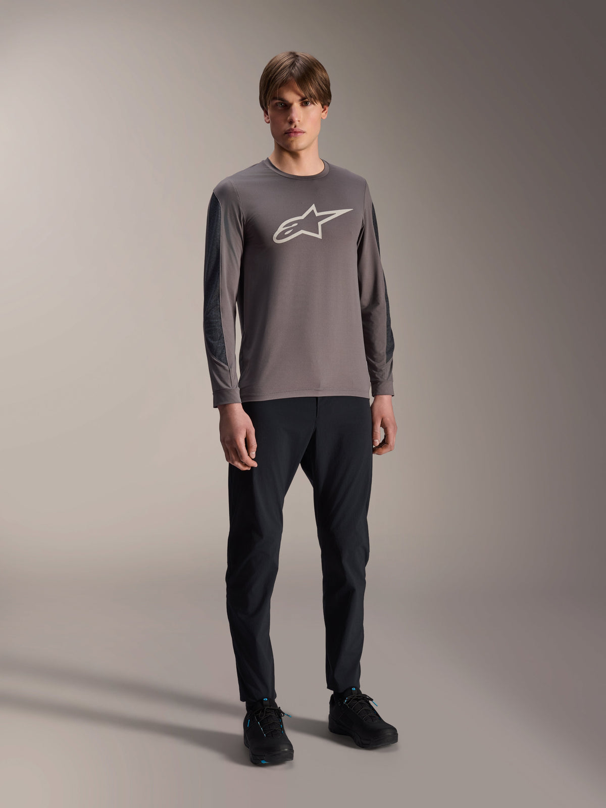 Alpinestars A-Dura Insert Astar Jersey, Long Sleeve MTB Jersey, Dark Gray, featuring large white chest logo, worn with black technical pants and black shoes, off-road cycling apparel