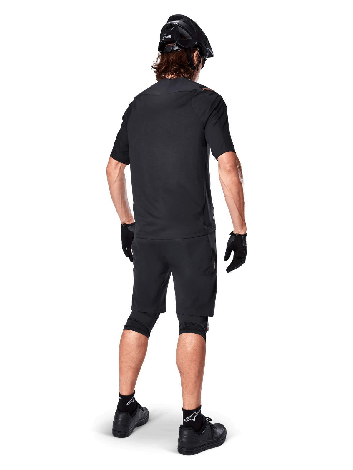 Kolarz górski widoczny od tyłu w czarnej koszulce Alpinestars A-Aria Polartec Switch z krótkim rękawem, czarne spodenki MTB, czarny kask i rękawiczki, profesjonalny zestaw sportowy do jazdy w terenie