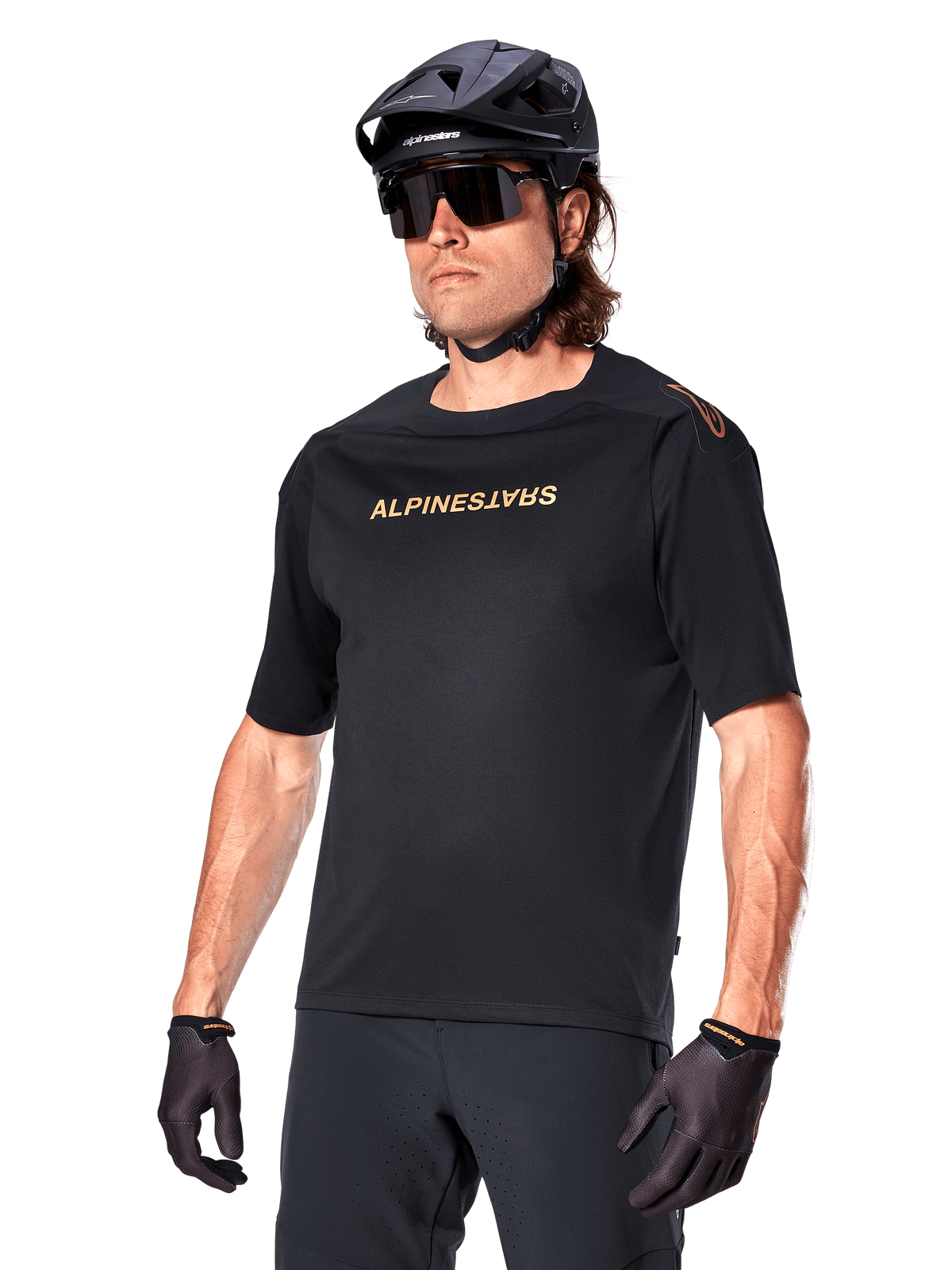 Alpinestars A-Aria Polartec Switch Jersey z krótkim rękawem, czarna koszulka rowerowa ze złotym brandingiem Alpinestars, czarny kask, okulary przeciwsłoneczne i rękawice, techniczna odzież MTB