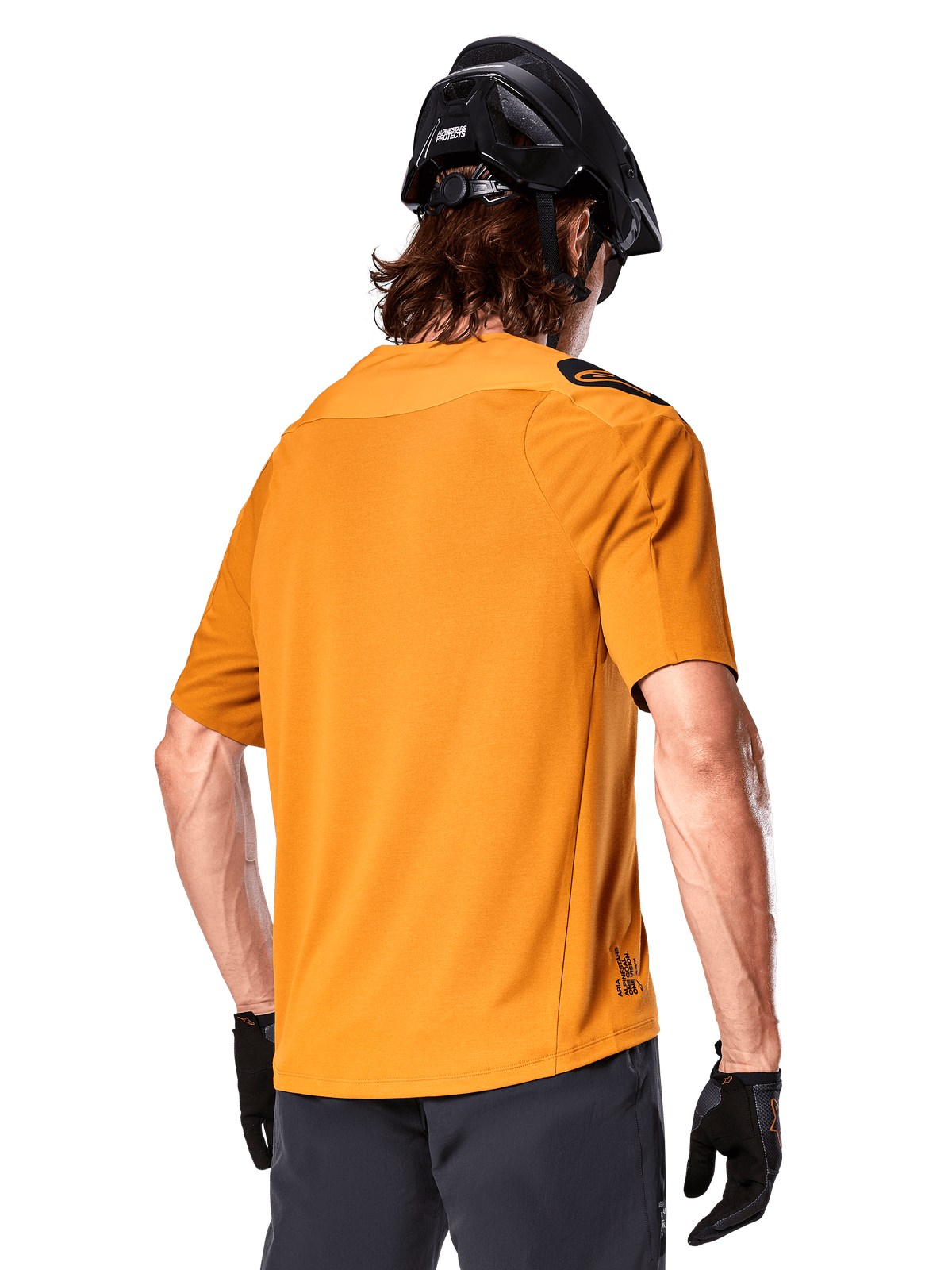 Alpinestars A-Aria Polartec Switch Jersey, koszulka MTB z krótkim rękawem, ciemnozłota, widok z tyłu ukazujący sportowe dopasowanie, zestawiona z czarnym kaskiem i szarymi szortami, wytrzymała i oddychająca odzież na szlaki