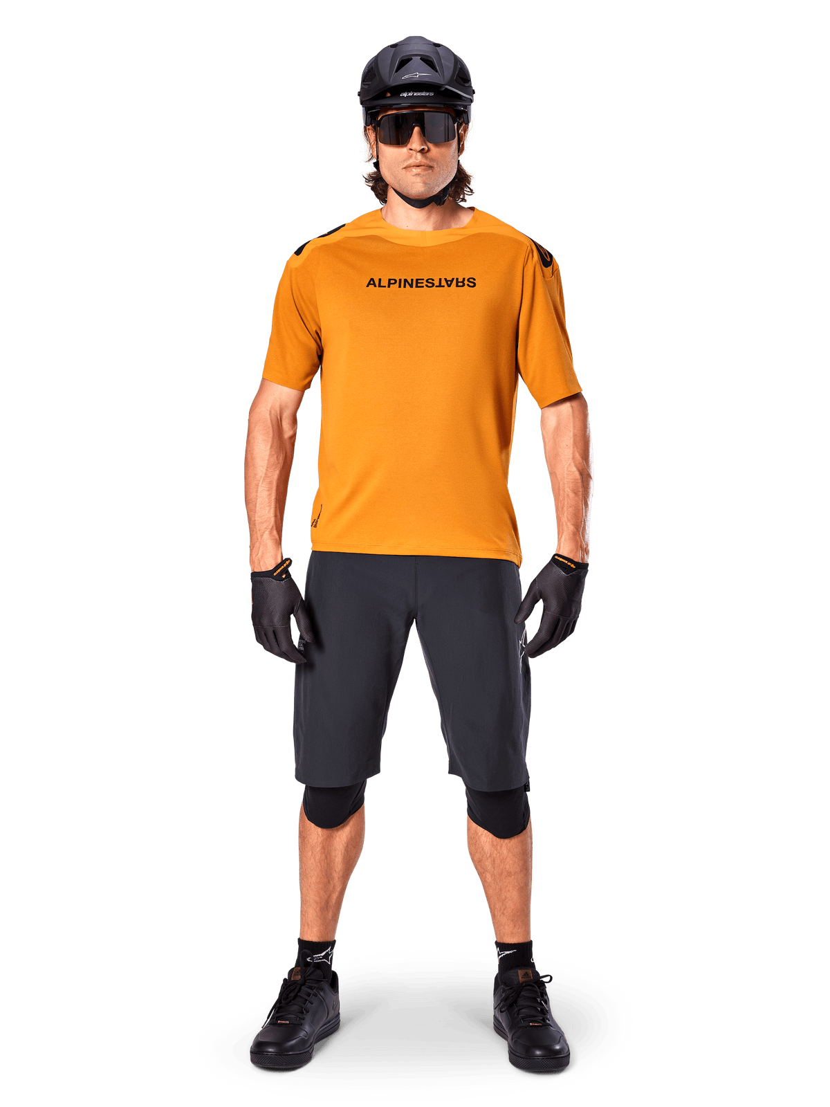Kolarz w koszulce Alpinestars A-Aria Polartec Switch z krótkim rękawem w kolorze Dark Gold, czarne szorty MTB, kask, okulary przeciwsłoneczne i rękawiczki, profesjonalny zestaw do jazdy na rowerze górskim