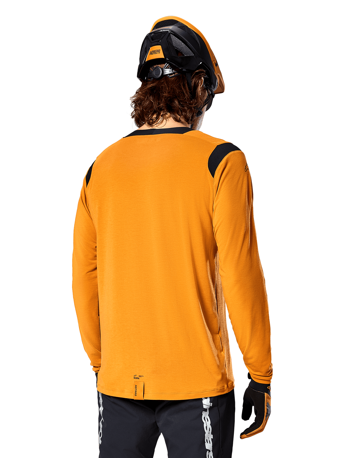 Alpinestars A-Dura Dri Wool Long Sleeve Jersey w kolorze Dark Gold, widok z tyłu na rowerzystę w kasku MTB i rękawiczkach, czarne panele z siatki na ramionach i przedłużony tył, techniczna odzież rowerowa do jazdy po szlakach
