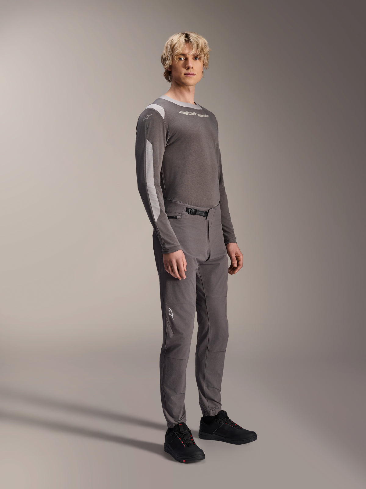 Alpinestars A-Dura Elite Pants, Mountain Bike Pants, Dark Gray, worn with a matching long-sleeve jersey and black shoes, featuring a front ratchet closure and durable Cordura fabric for trail and enduro riding