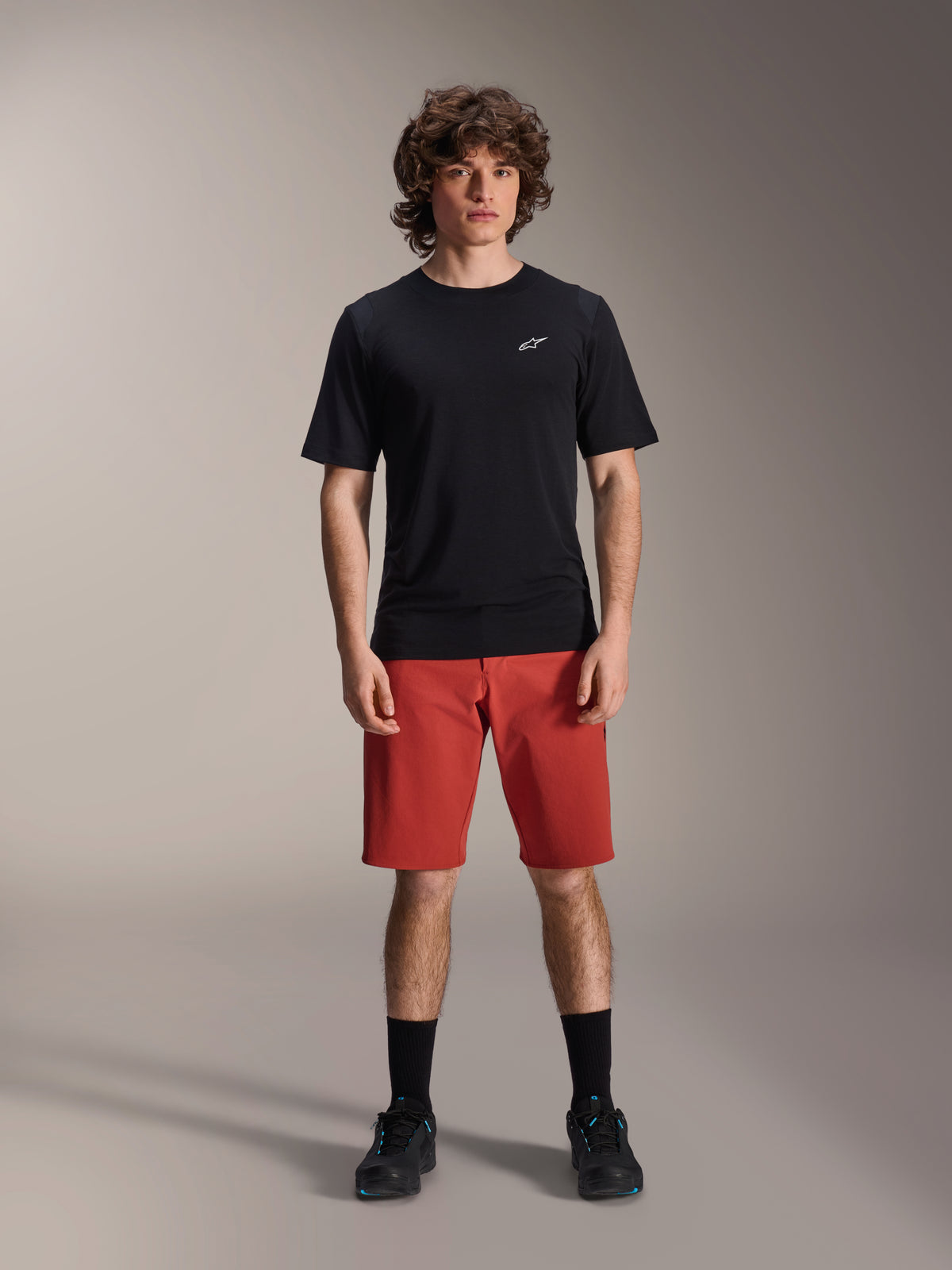 Alpinestars A-Dura Elite Shorts, spodenki rowerowe MTB, ciemnopomarańczowe, noszone z czarną koszulką z krótkim rękawem i butami rowerowymi, techniczna odzież do kolarstwa górskiego